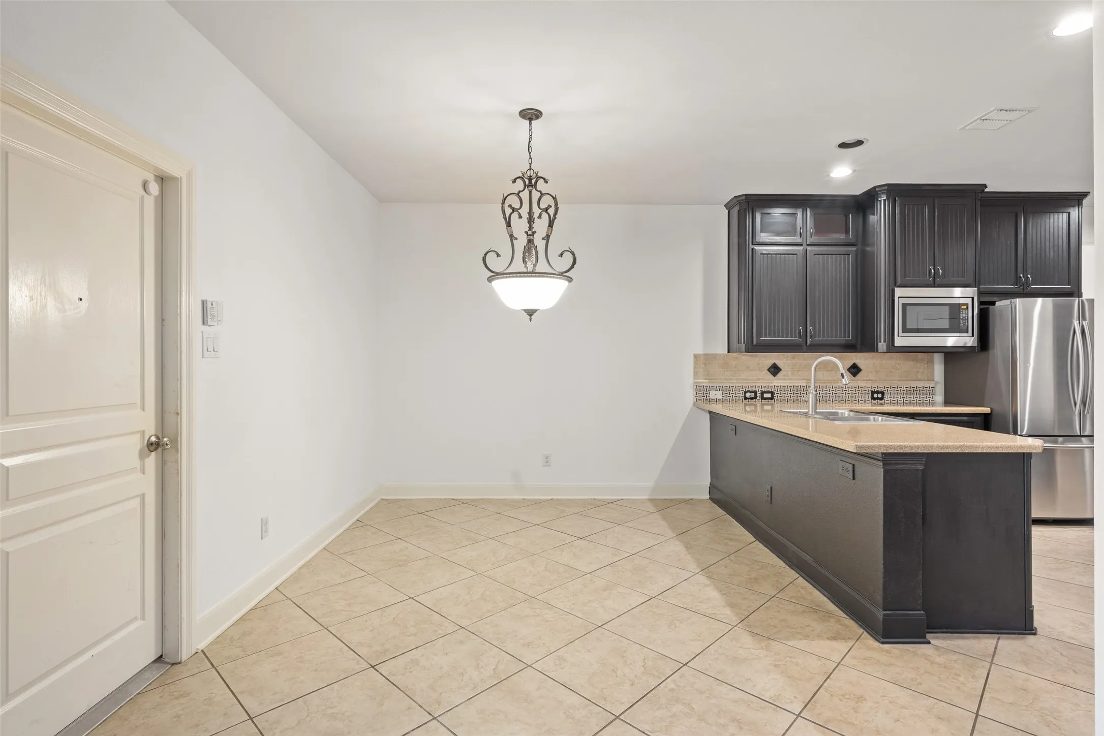Kitchen with light tile flooring, kitchen peninsula, stainless steel appliances, sink, and tasteful backsplash
