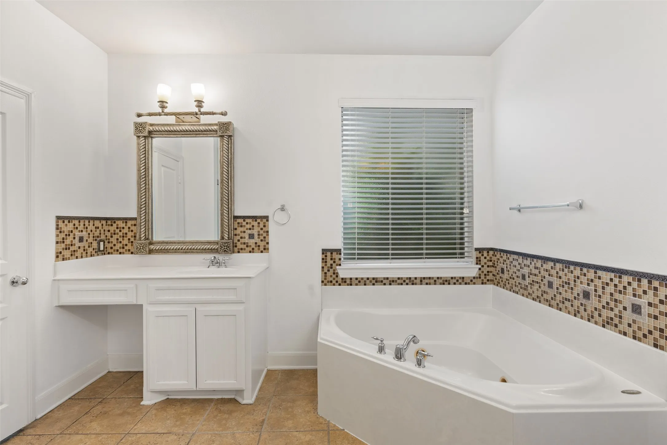 Bathroom featuring tile flooring, tasteful backsplash, vanity with extensive cabinet space, and a bath to relax in