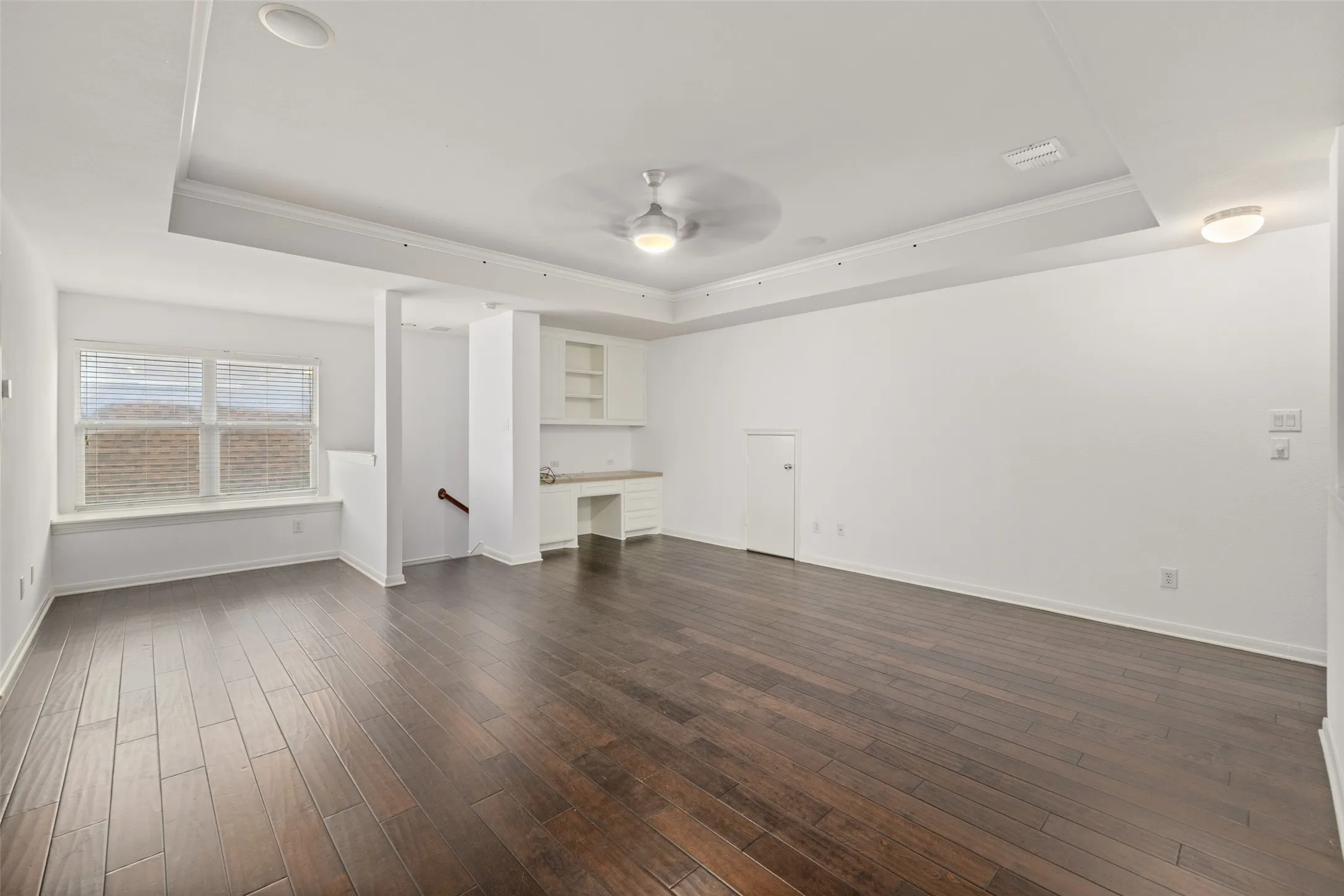 Unfurnished living room featuring dark wood-type flooring, ceiling fan, and a tray ceiling