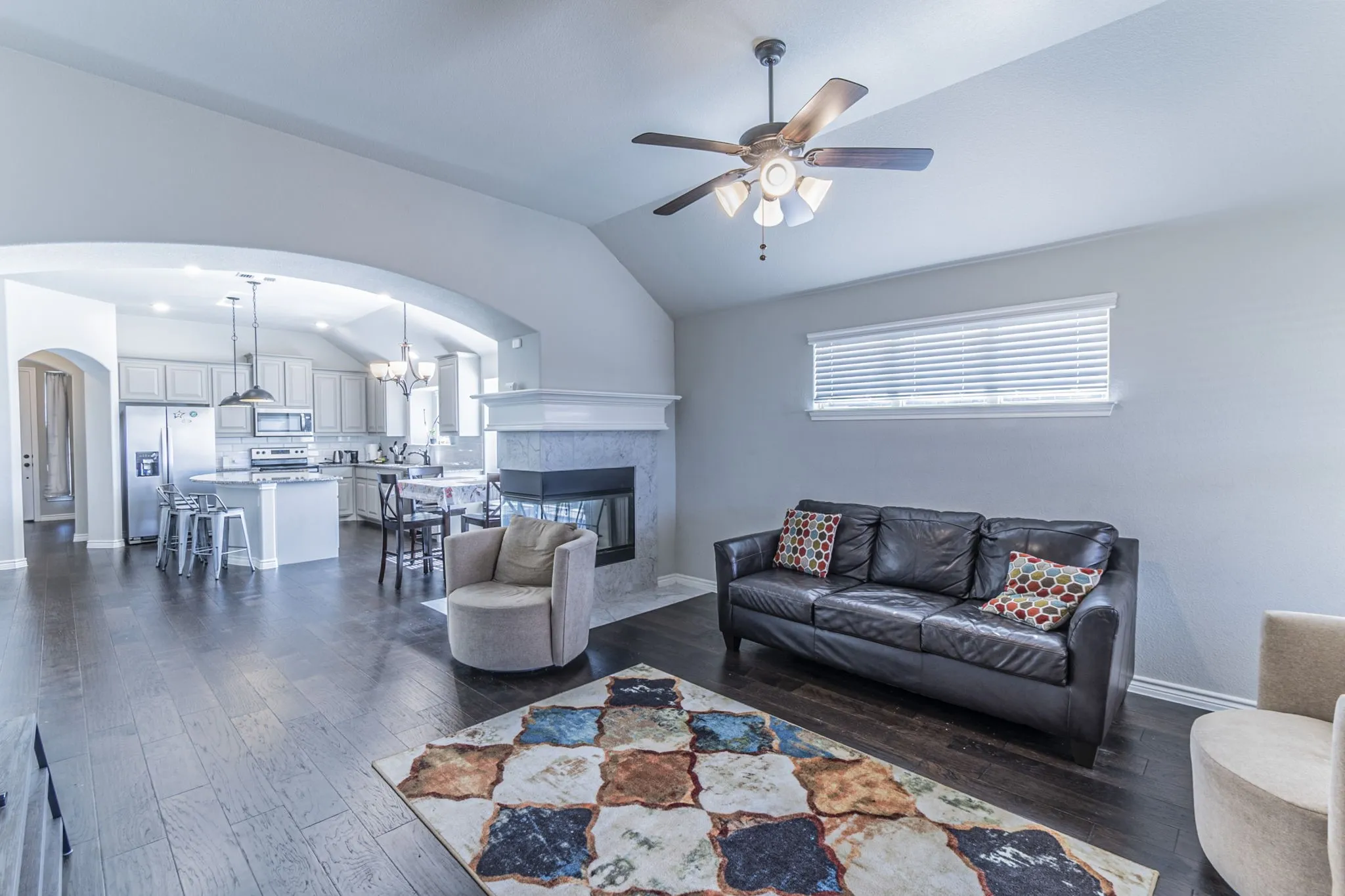 Spacious living area featuring wood-finish flooring, a ceiling fan, and a fireplace with a light-colored mantel