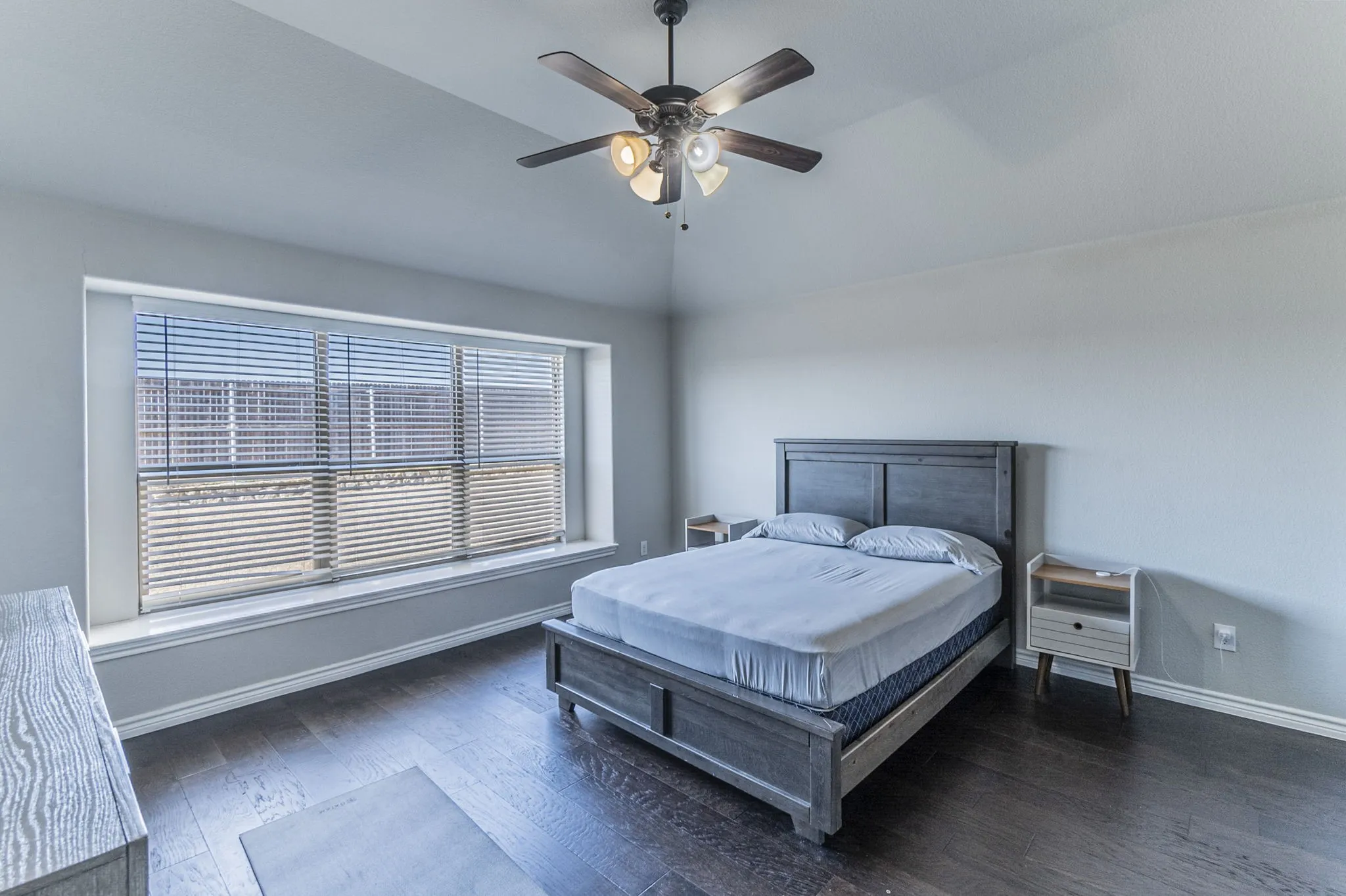 Spacious room featuring dark wood-finish flooring, a large window with horizontal blinds, and a built-in window ledge