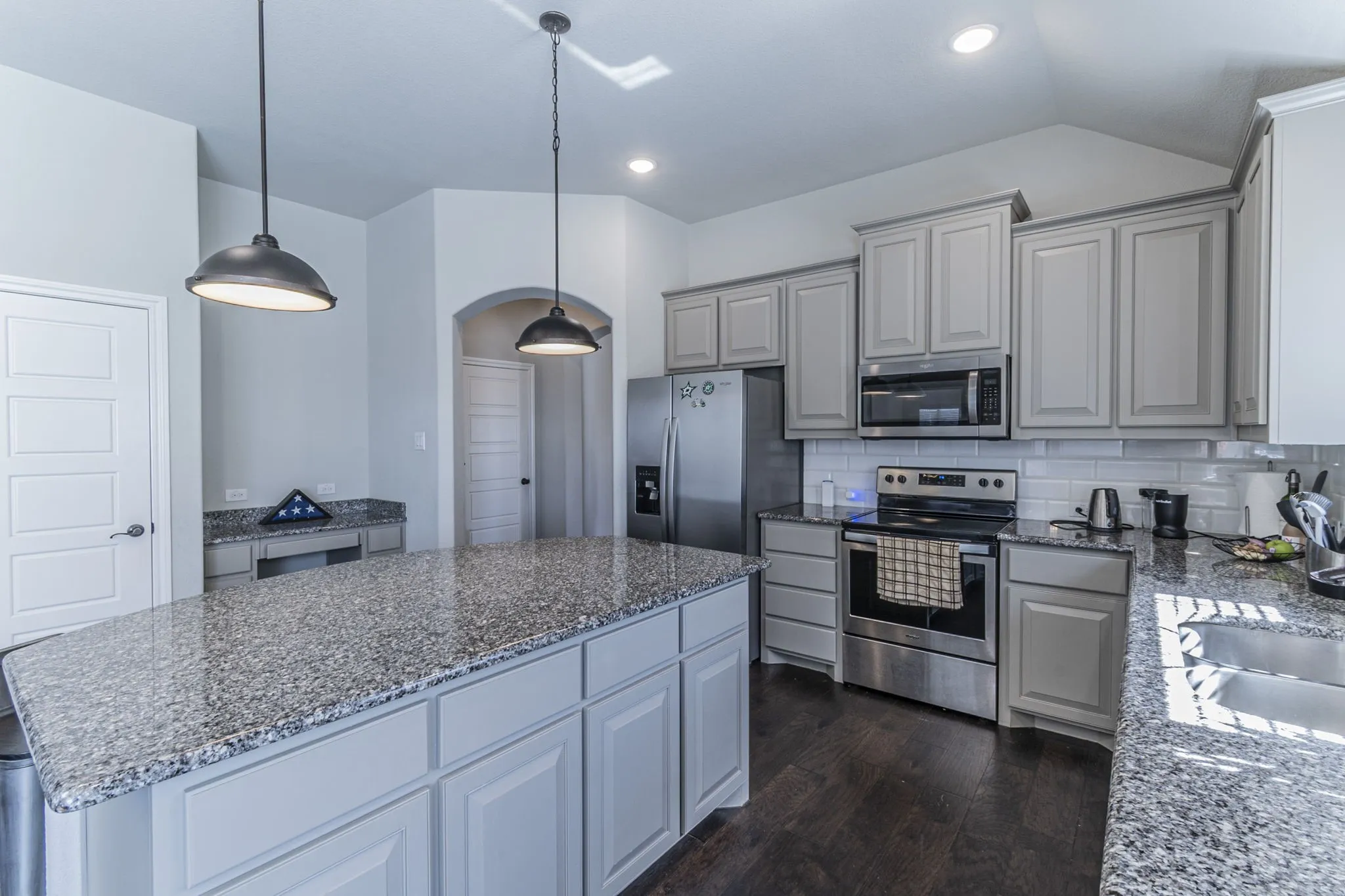 Kitchen featuring an expansive island with granite countertops, light gray cabinetry, stainless steel appliances, and dark wood-finish flooring