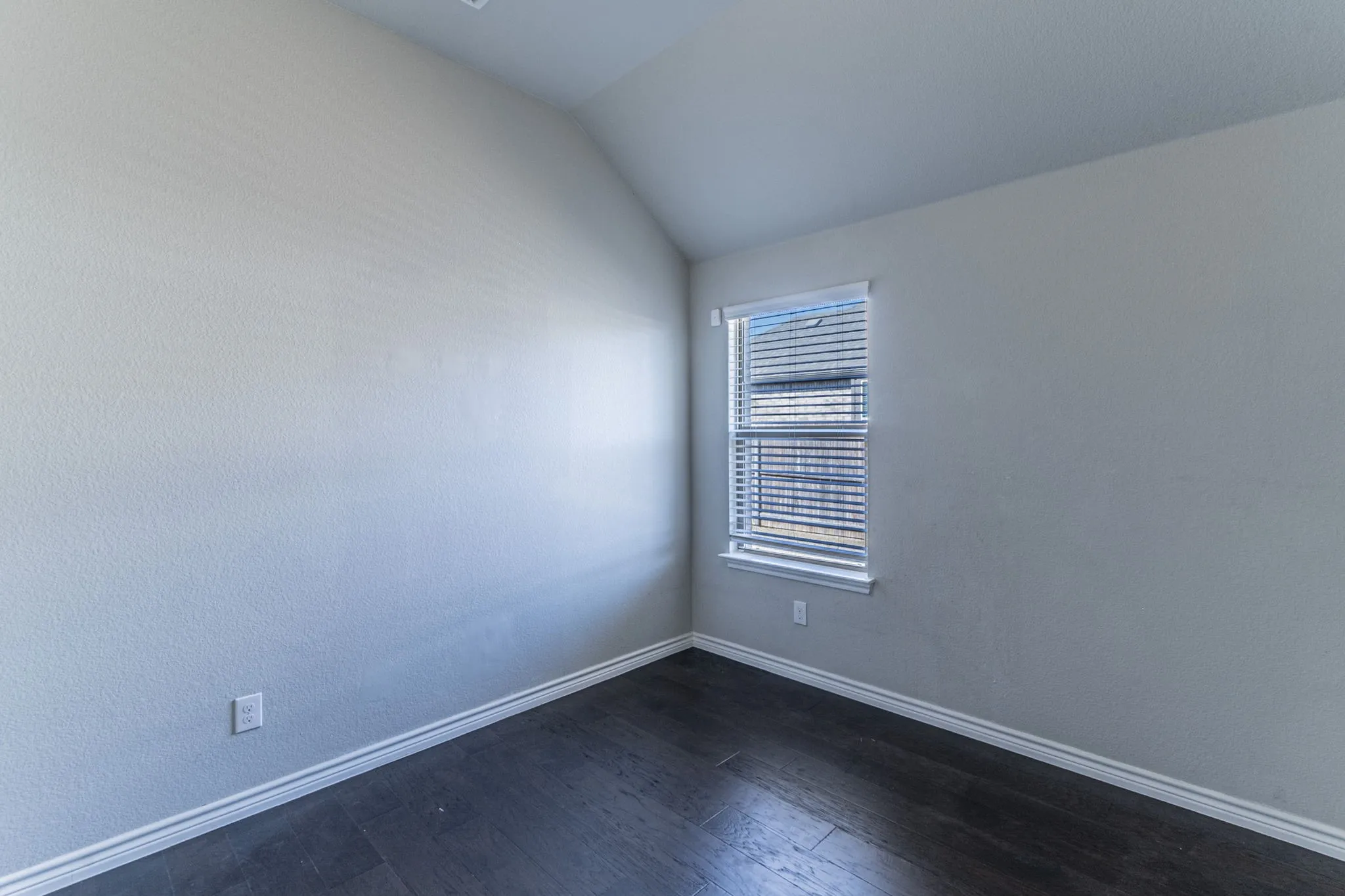 Room with wood-finish flooring, light grey walls, and white baseboards