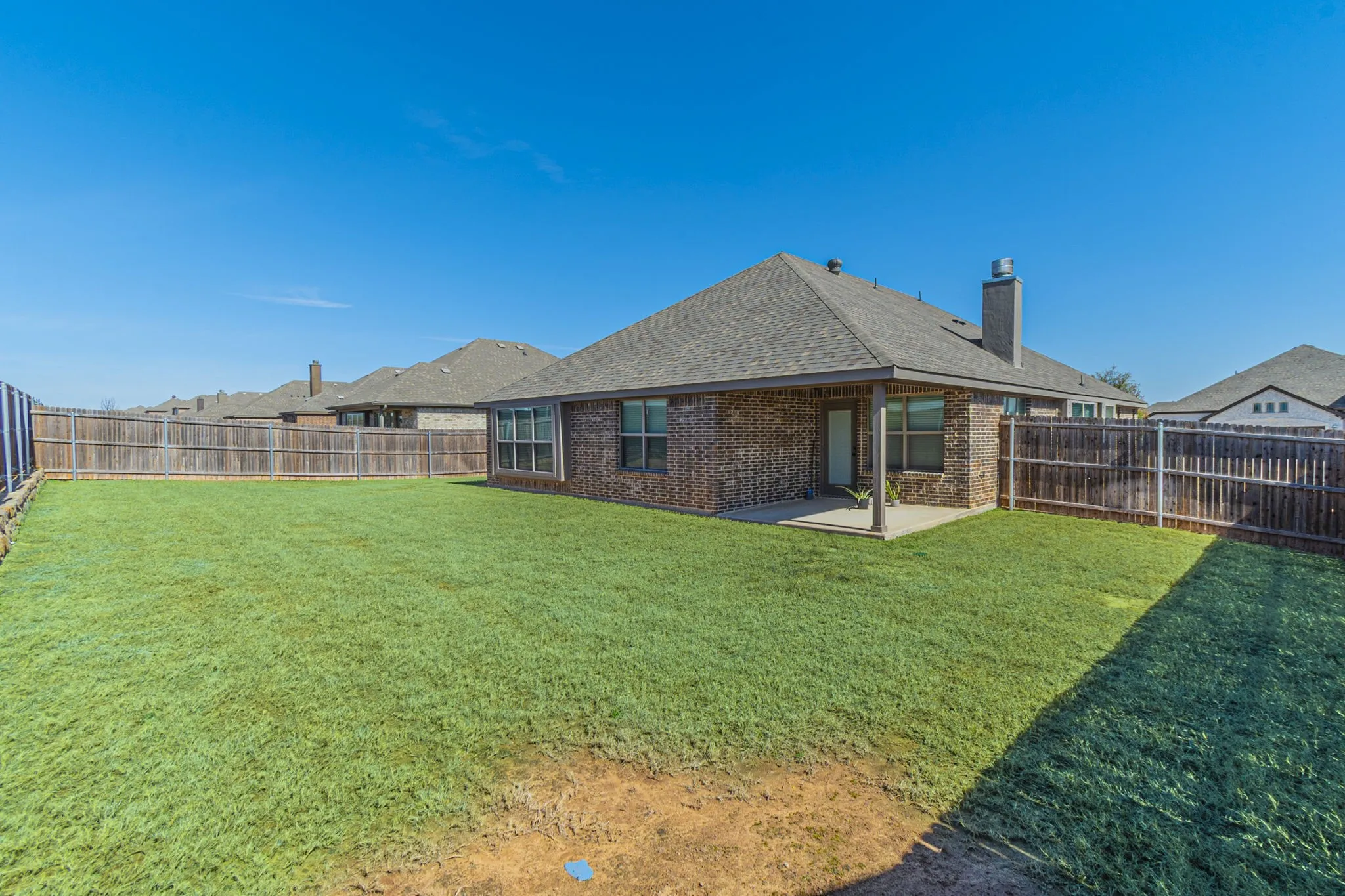 Expansive backyard with a lush green lawn, full privacy fencing, and a covered patio