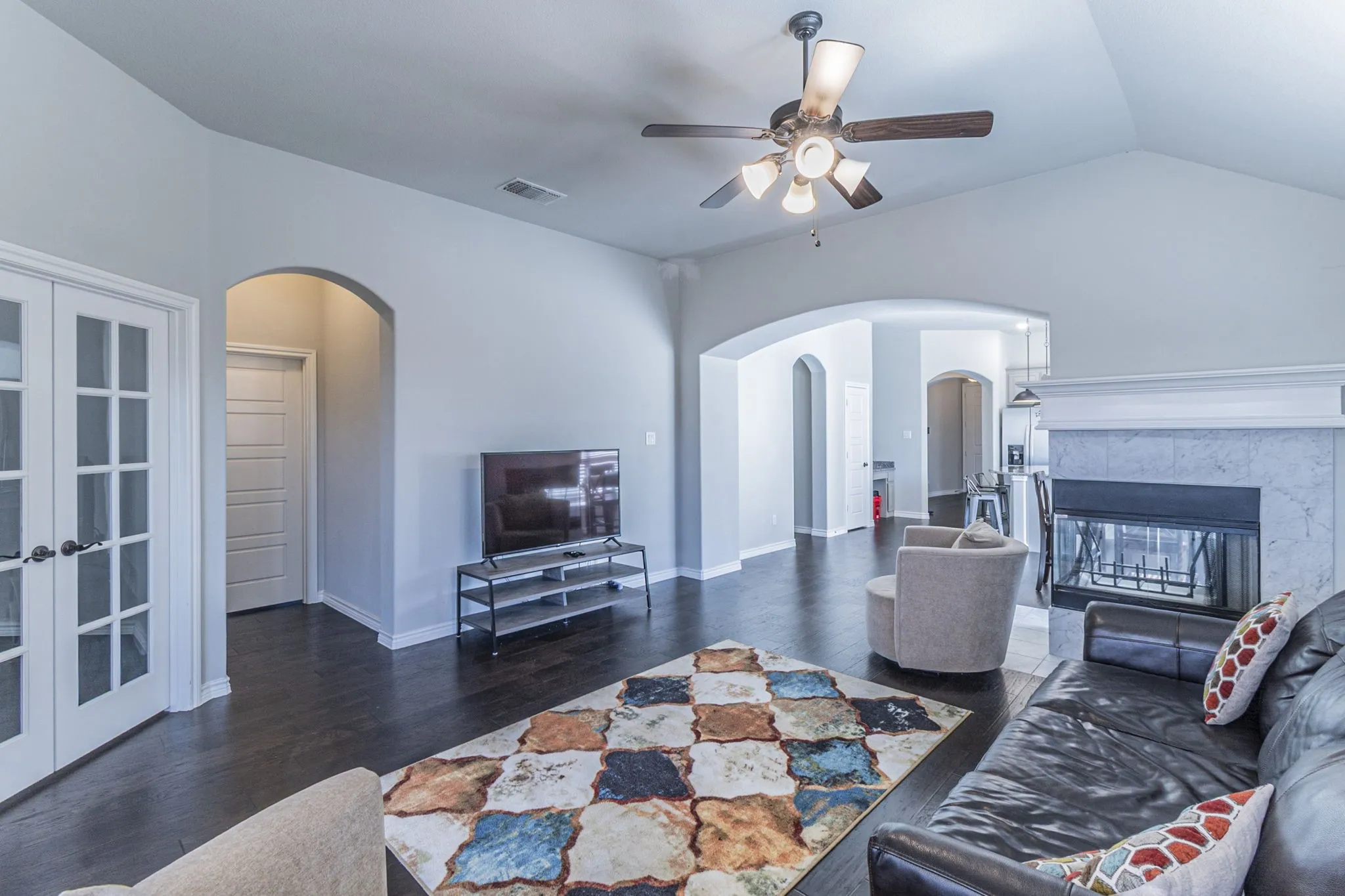 Spacious living area featuring vaulted ceilings, dark wood-finish flooring, and a fireplace with a light-colored tile surround and white mantel