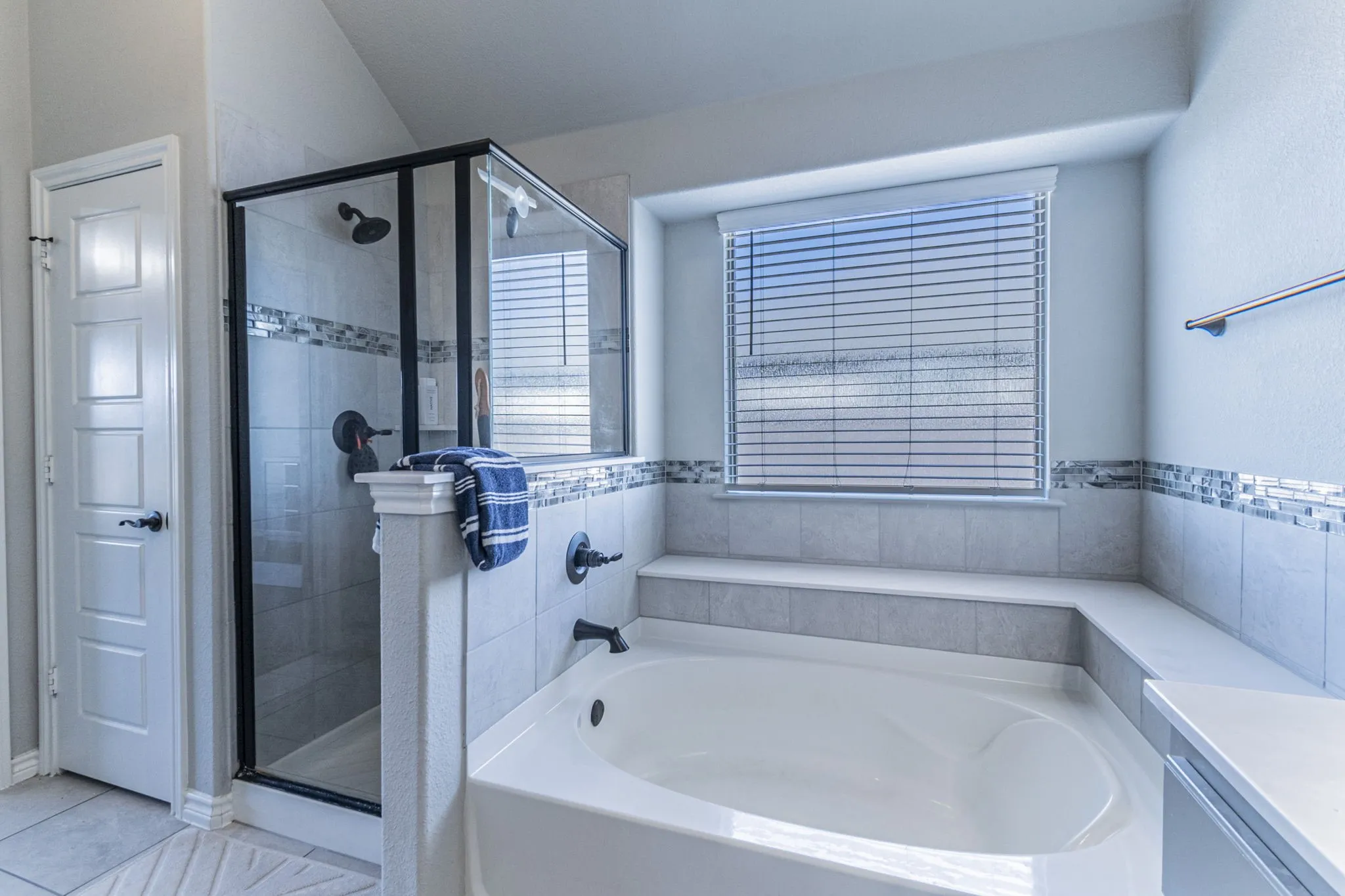 Built-in soaking tub with a tiled surround, complemented by a walk-in shower featuring a glass enclosure and dark bronze fixtures