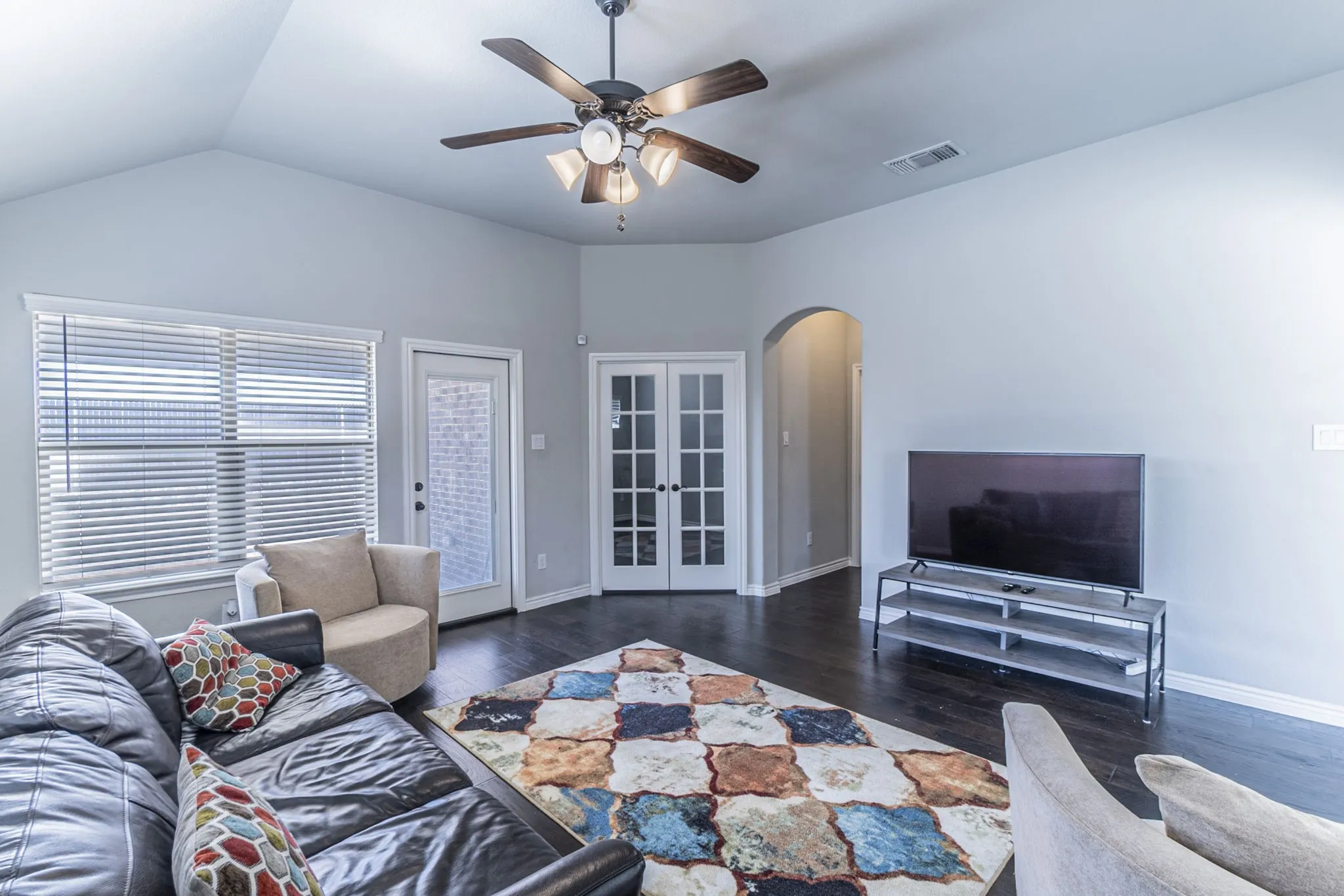 Living area featuring a vaulted ceiling with ceiling fan, dark wood-finish flooring, and light gray wall paint