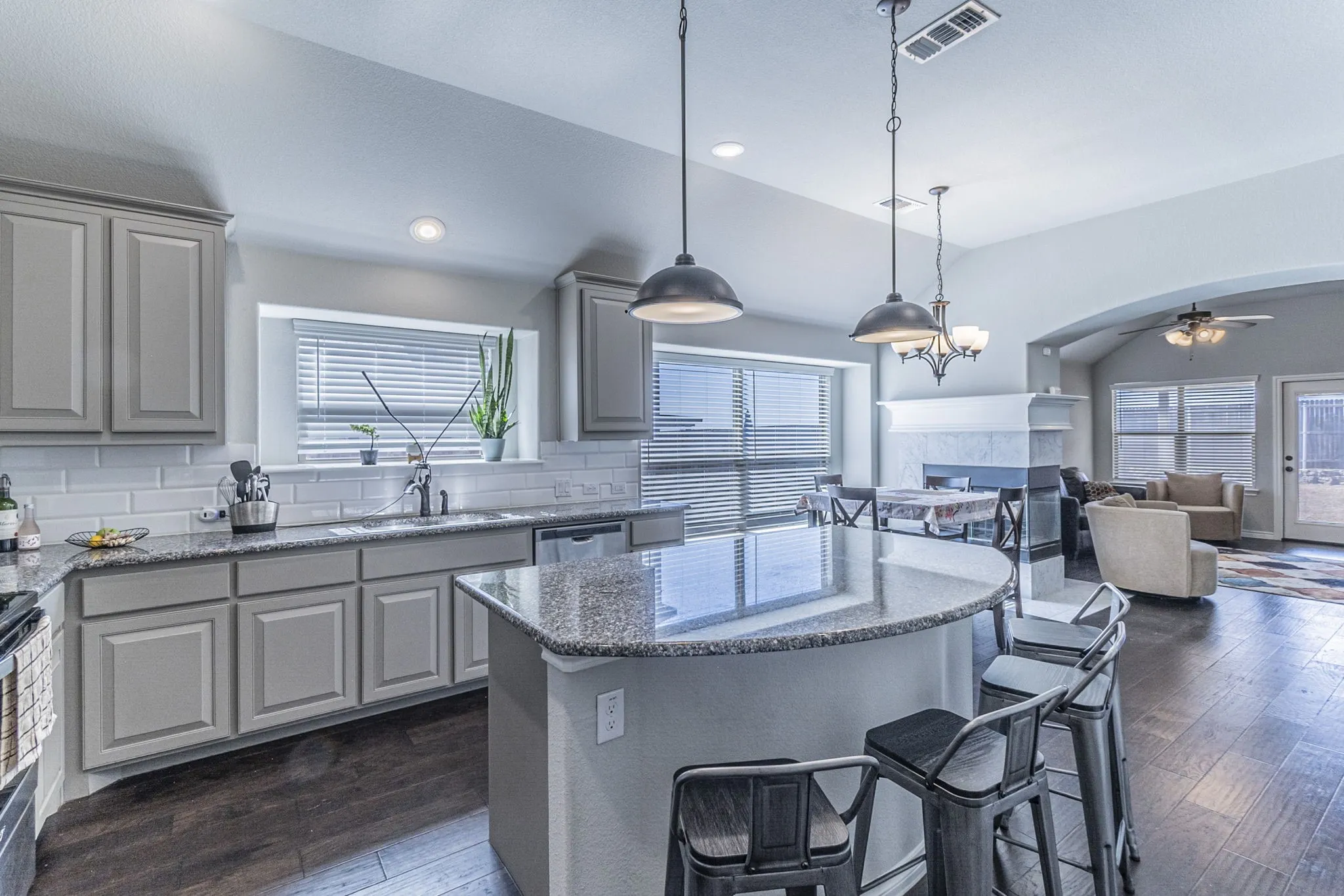 Modern kitchen featuring light gray cabinetry, subway tile backsplash, and a large central island with a granite-style countertop