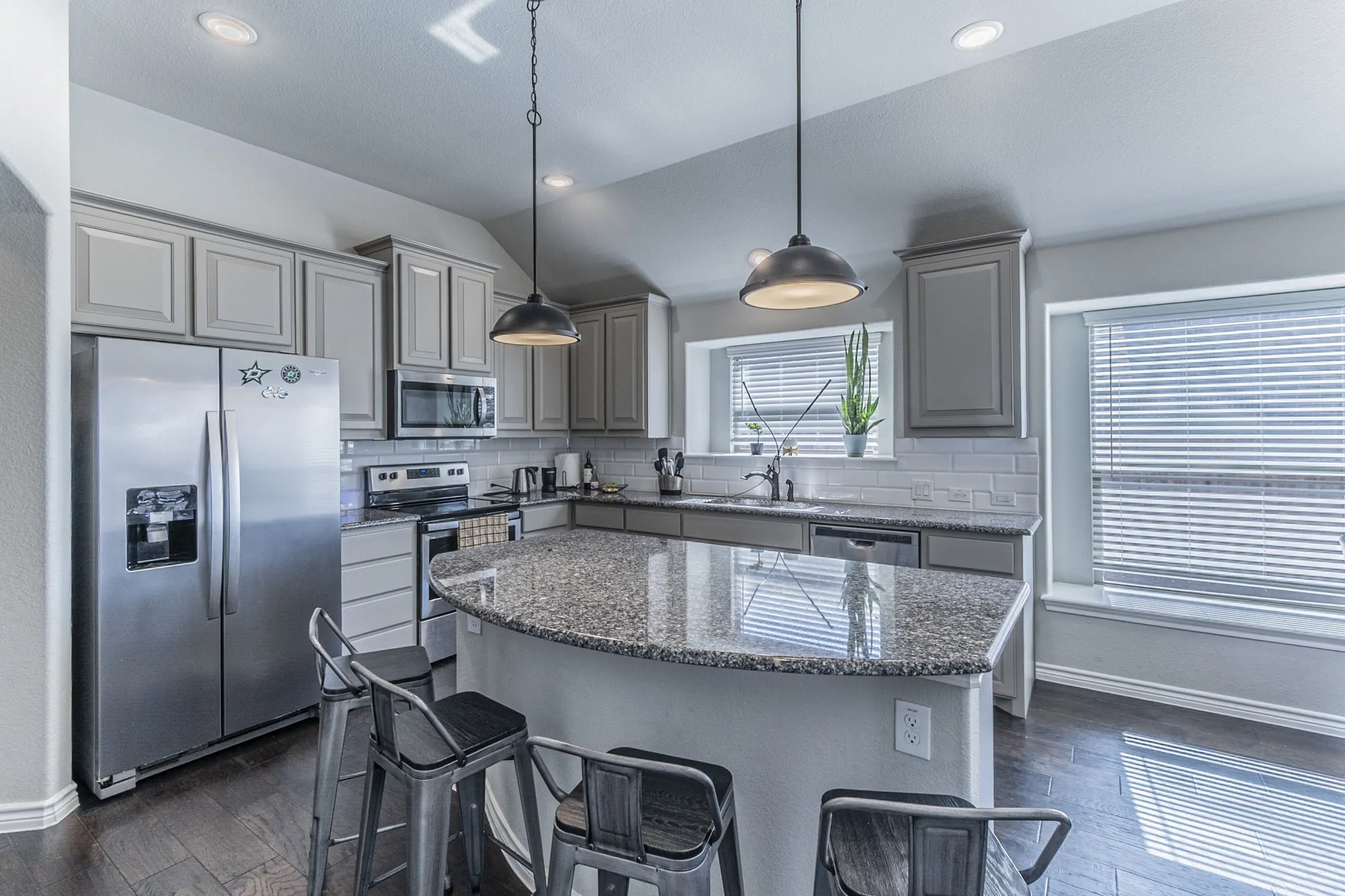 Kitchen featuring a large island with a stone countertop, recessed lighting, pendant lighting, shaker-style cabinetry, and wood-finish flooring