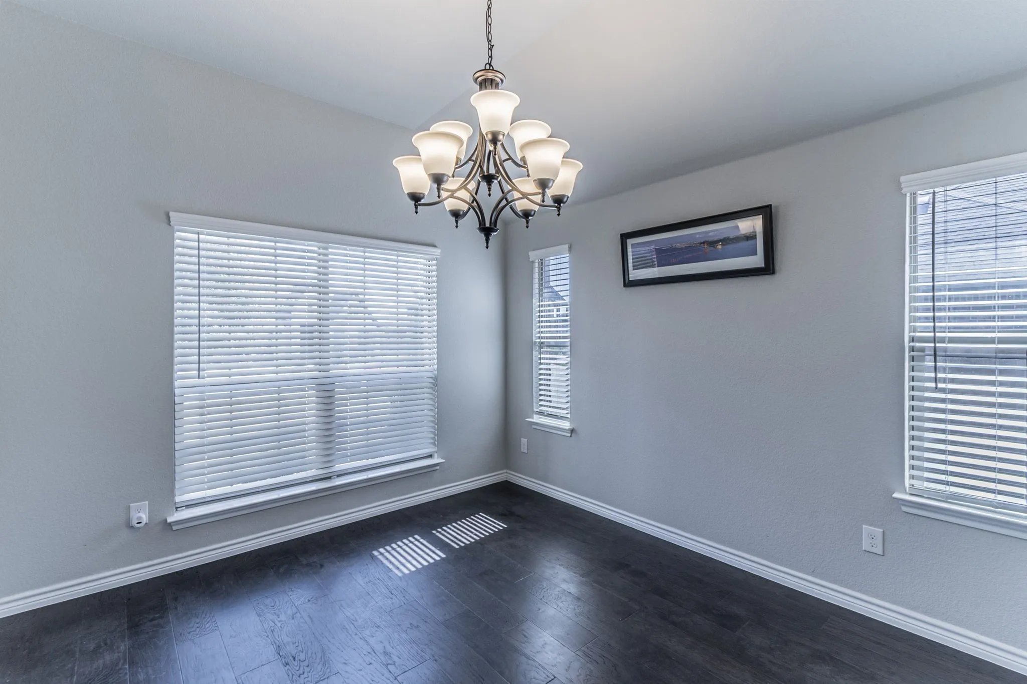 Spacious room featuring dark wood-finish flooring, light grey walls, and white baseboards