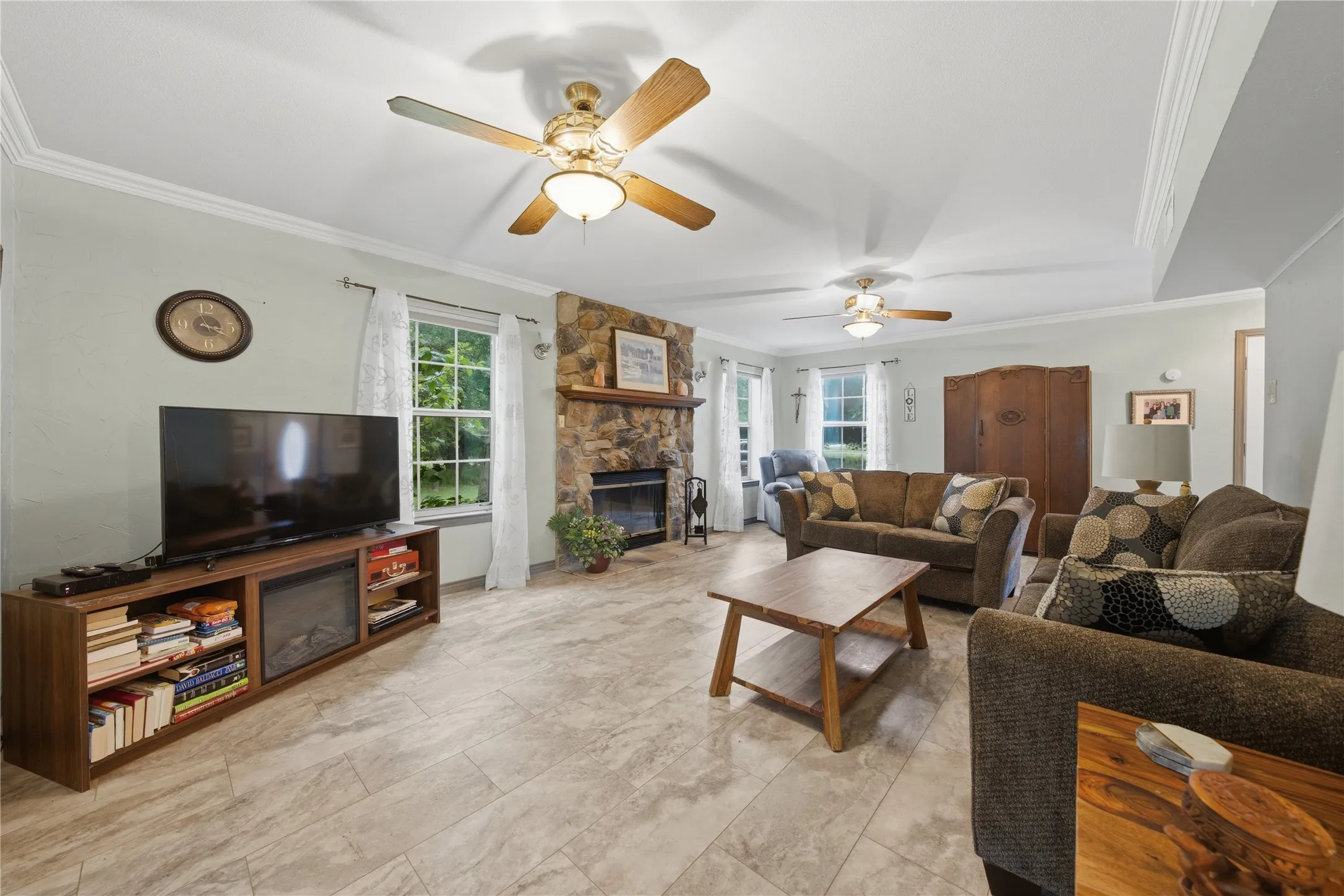 Spacious living area featuring tile flooring, a stone-front fireplace with a wood mantel, and multiple windows