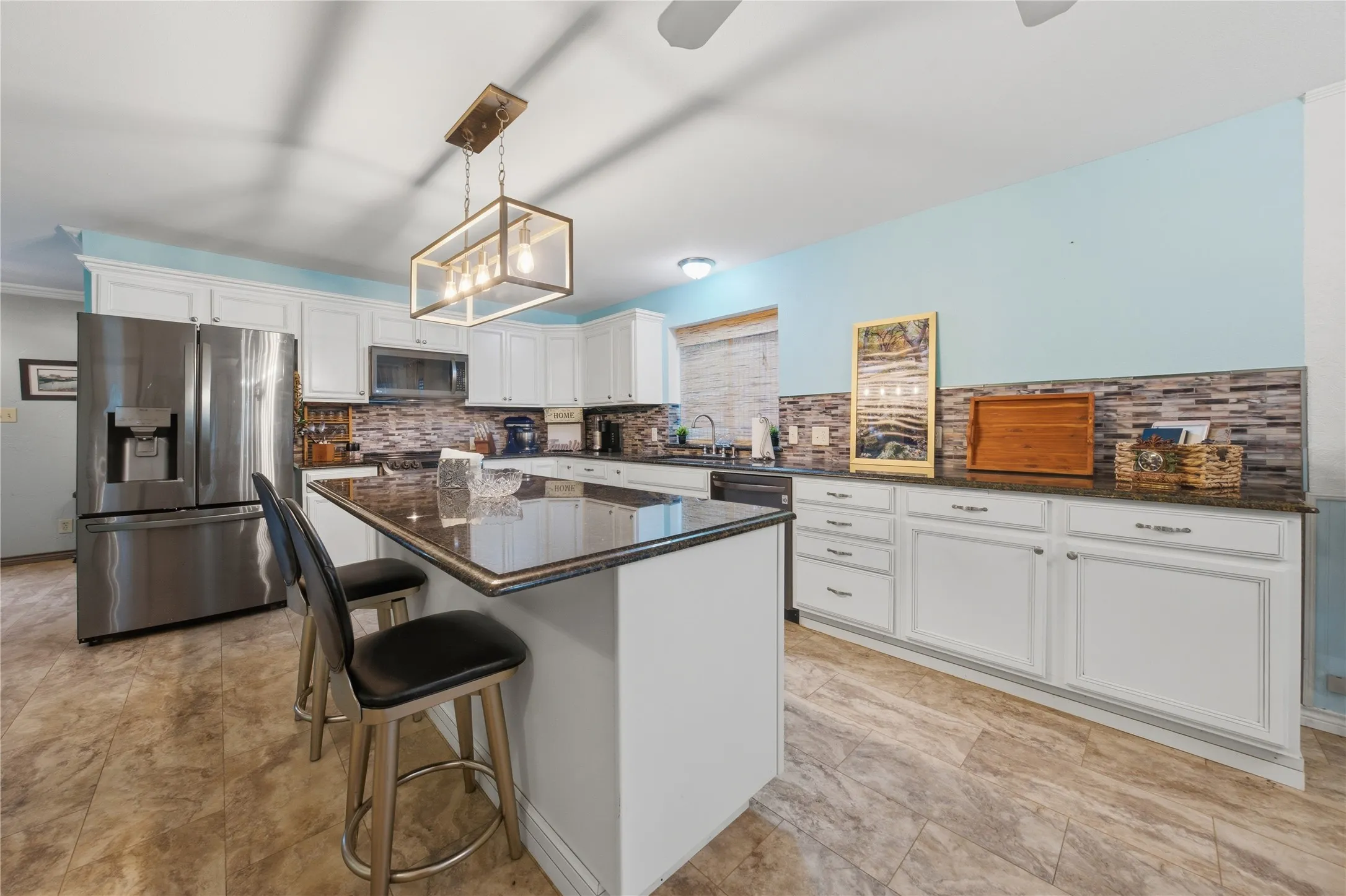Kitchen featuring an island with seating, dark countertops, white cabinetry, stainless steel appliances, and a mosaic tile backsplash