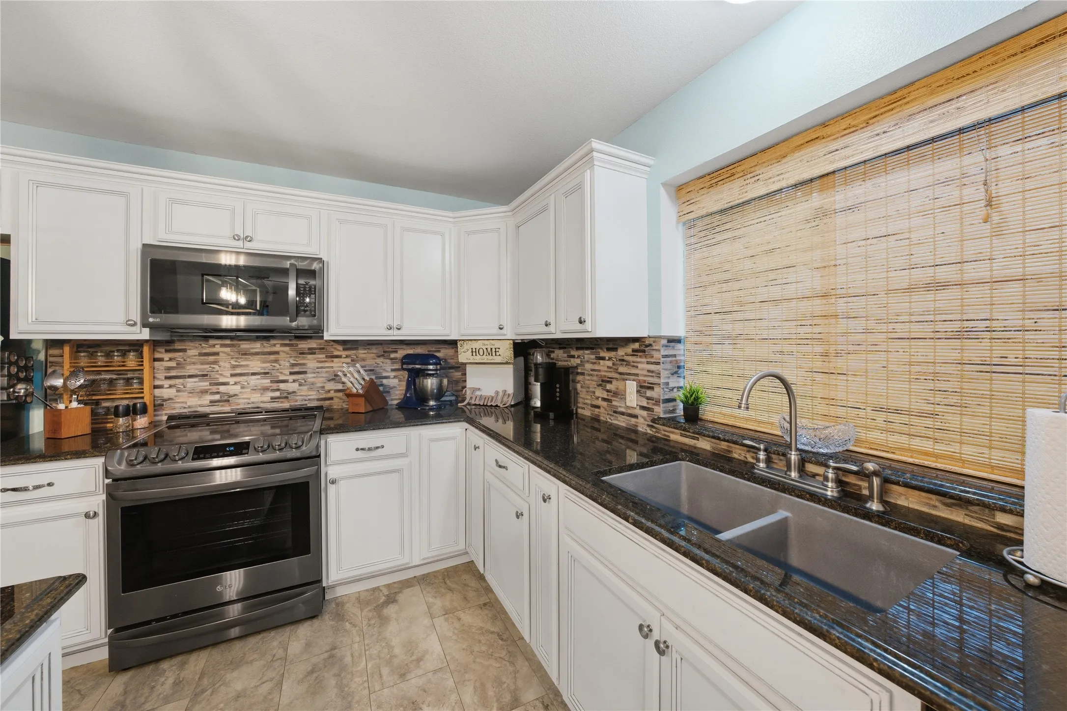 Well-appointed kitchen featuring white cabinetry, dark stone countertops, and a mosaic tile backsplash