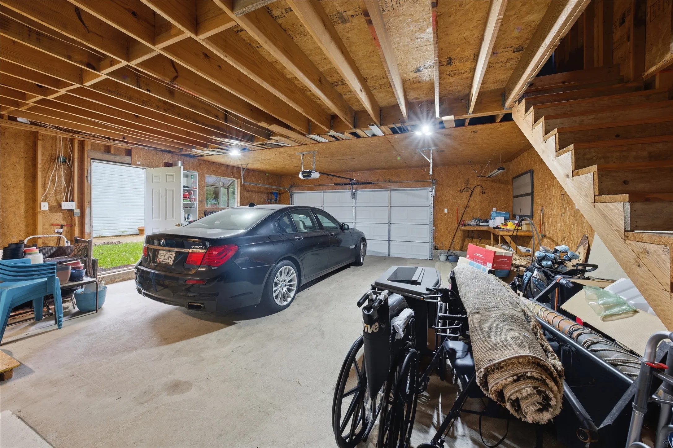 Spacious garage with exposed wood framing, concrete flooring, dual overhead garage doors, and an interior access door