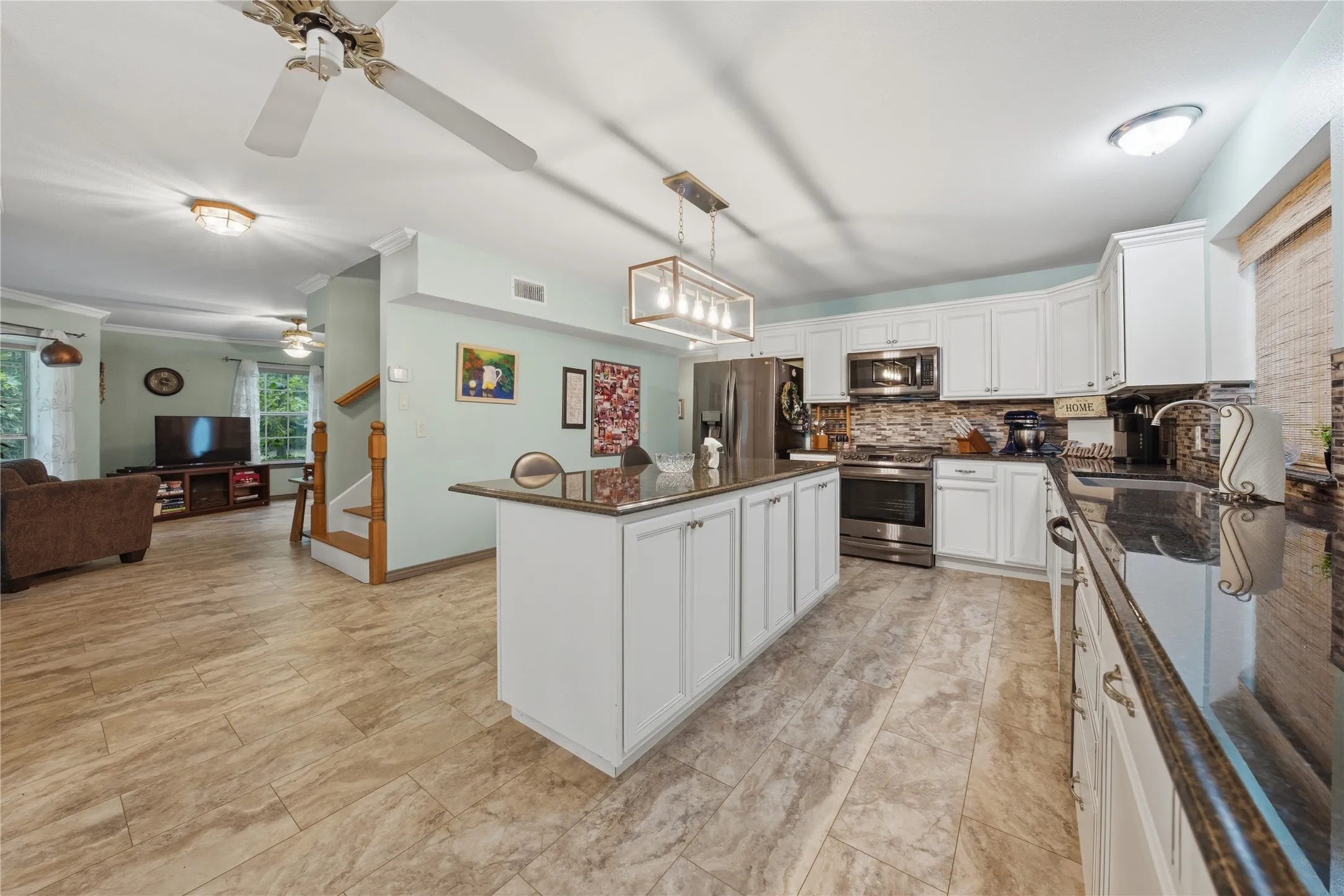Kitchen featuring white cabinetry, dark countertops, stainless steel appliances, and a central island with storage