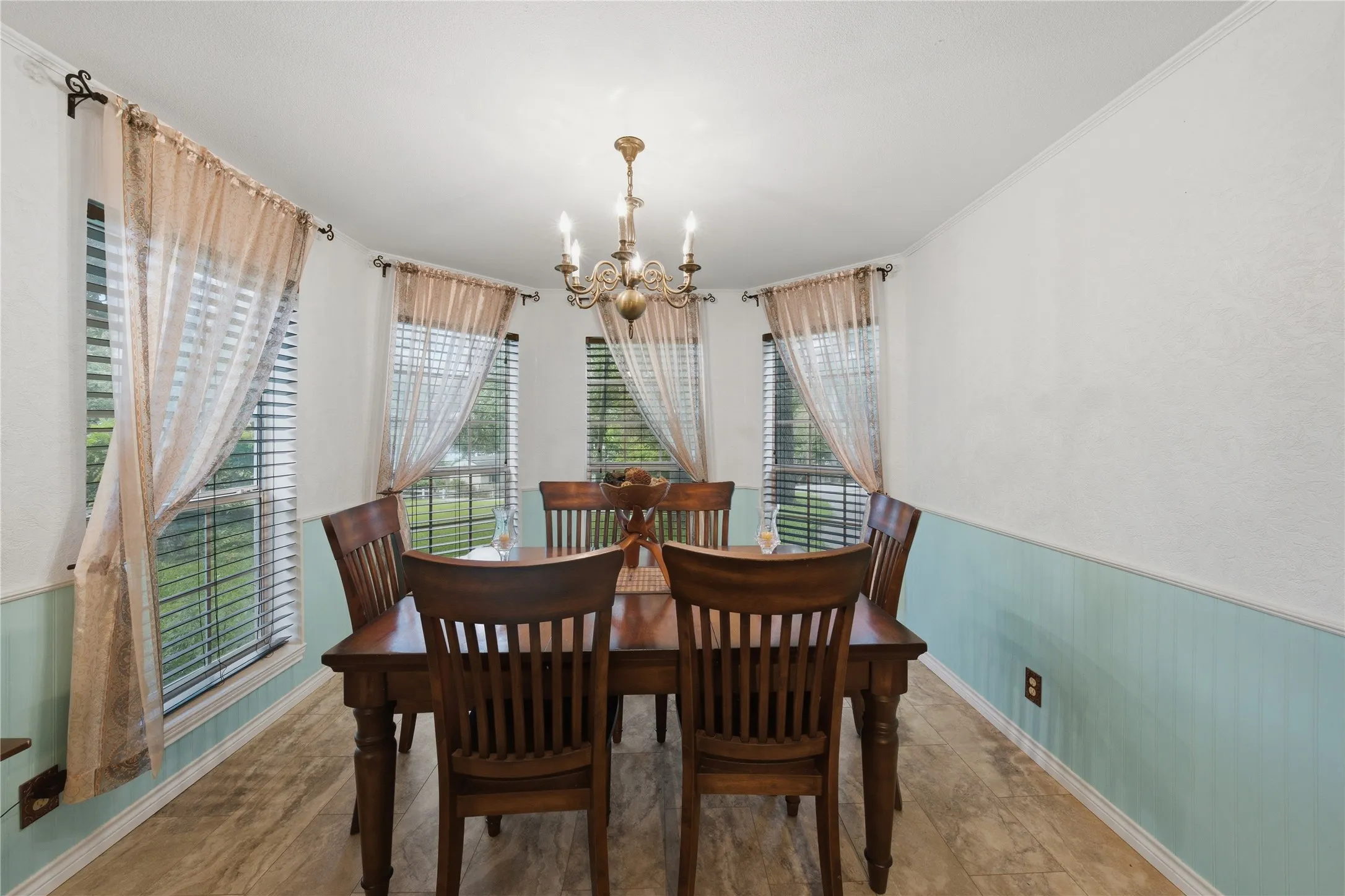 Dining area featuring a classic chandelier, paneled wainscoting, decorative wall texture, and multiple windows with blinds