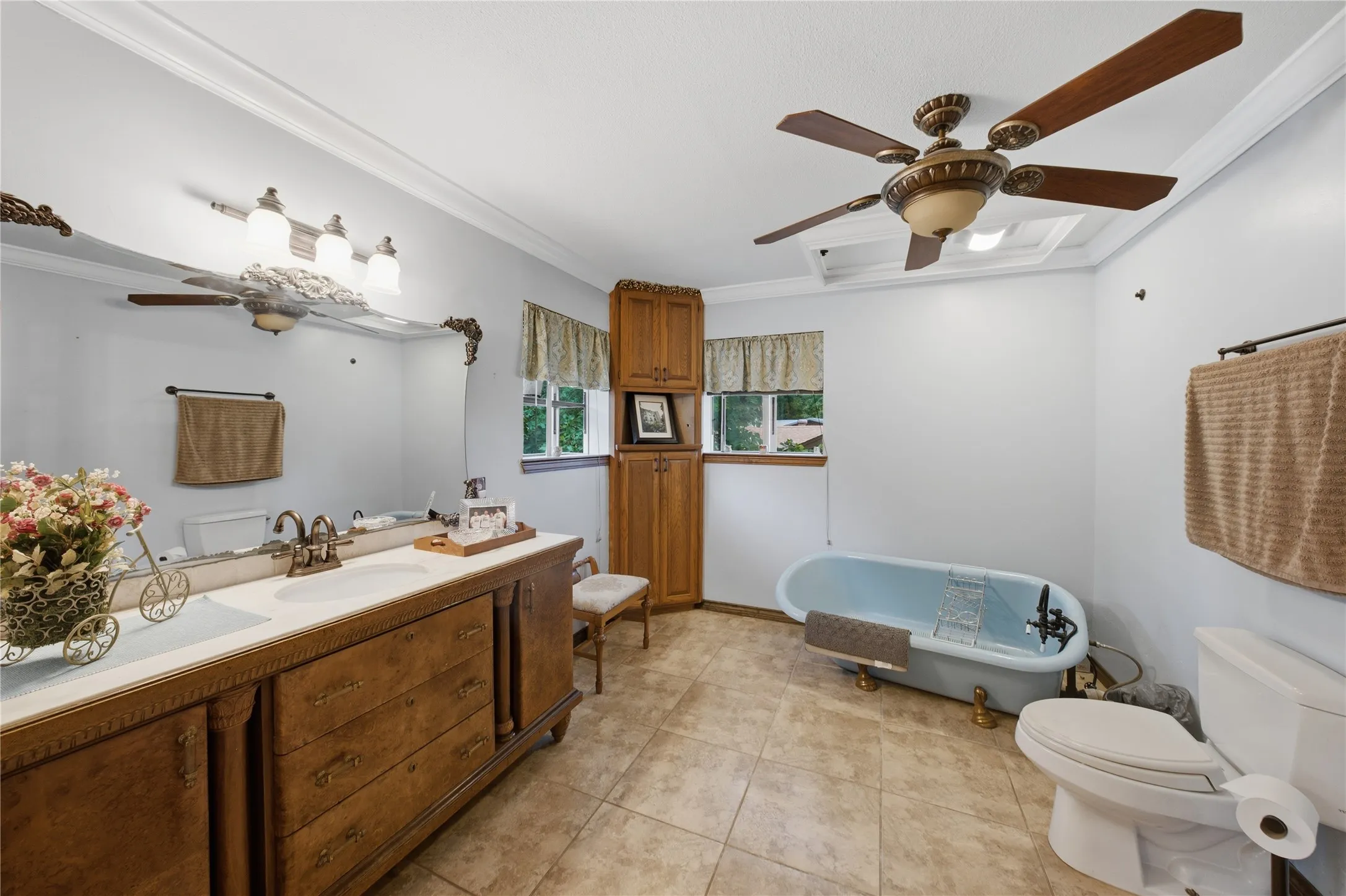 Bathroom featuring a double vanity with an ornate wood-finish base and dual sinks, a clawfoot soaking tub, tile flooring, and a ceiling fan