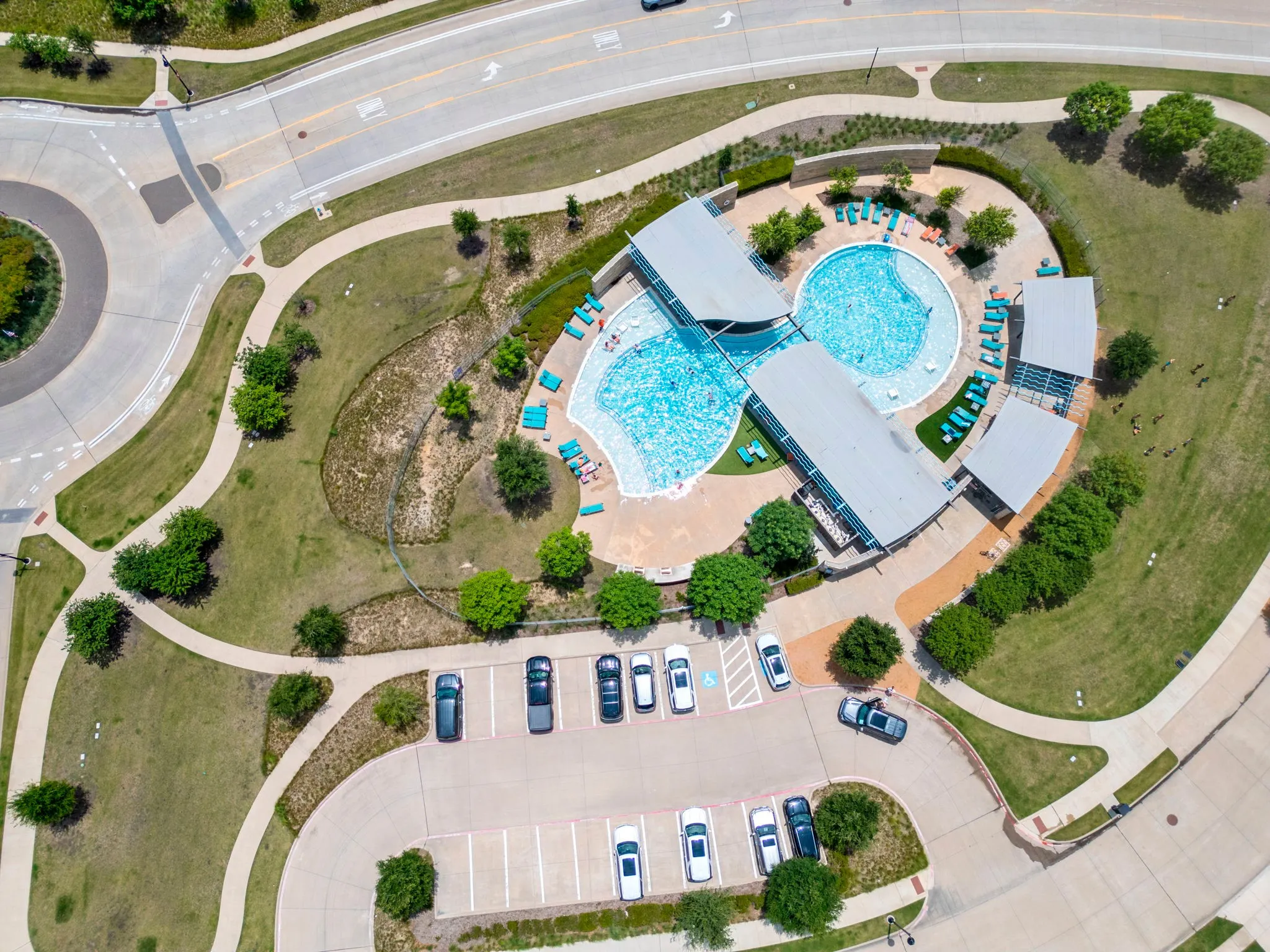 Community amenity center featuring a resort-style swimming pool with integrated shade structures, surrounded by ample lounging areas, pedestrian pathways, and dedicated parking