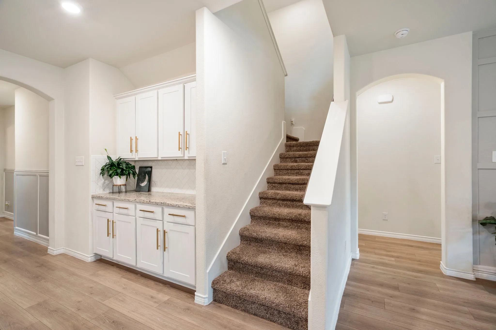 Staircase with carpeted treads and white risers, complemented by wood-finish flooring