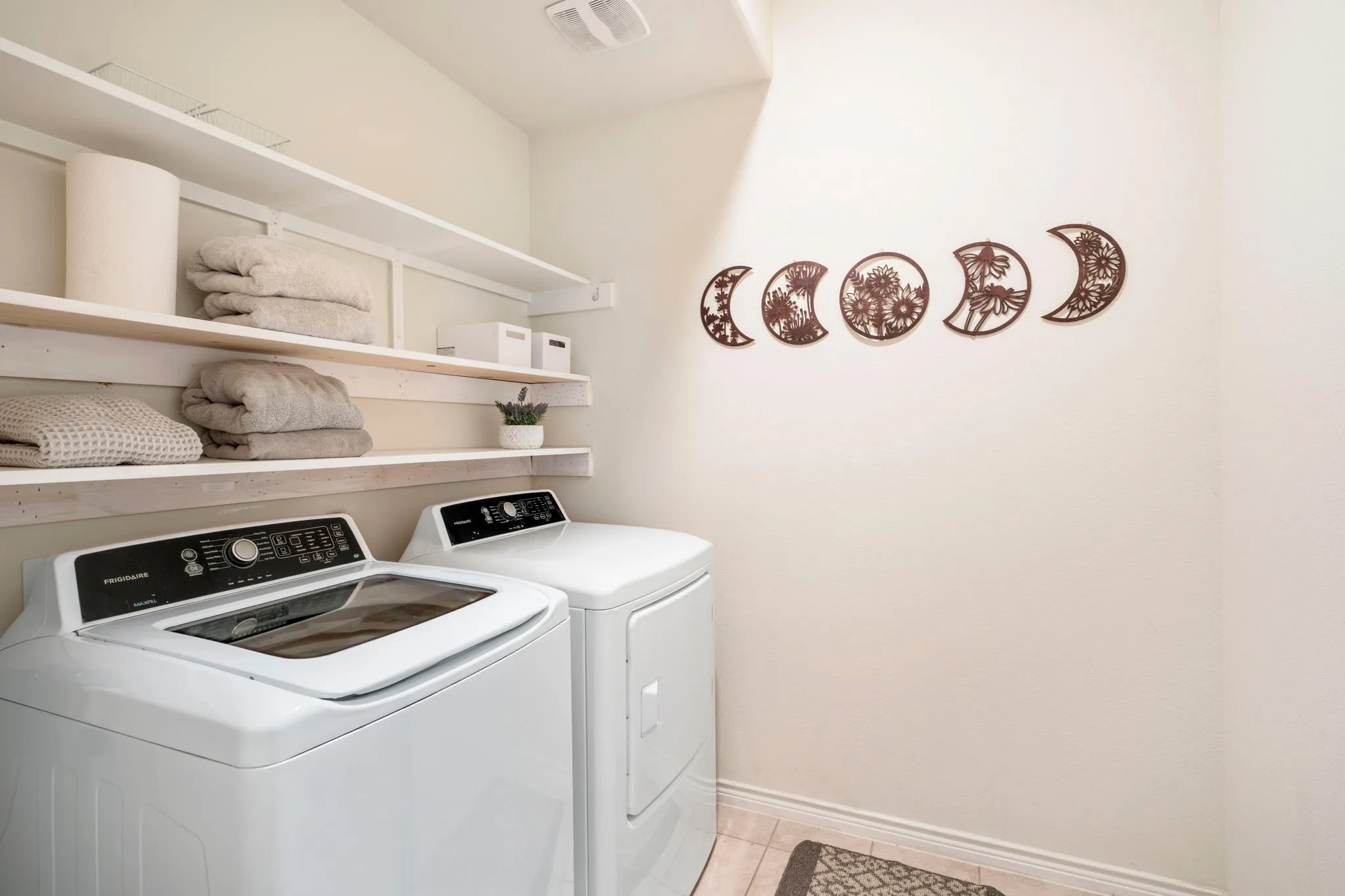 Dedicated laundry area featuring a top-load washer, front-load dryer, and multiple open shelving units for organization