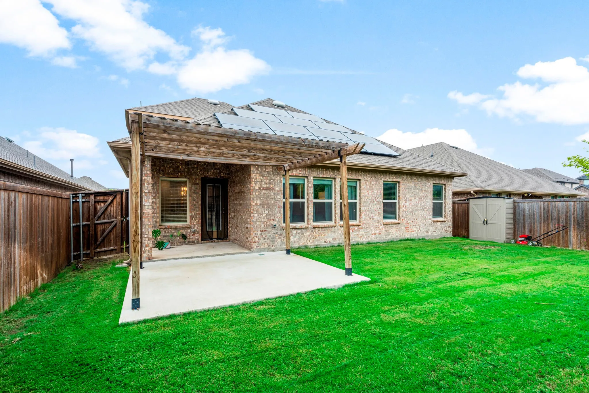 Expansive backyard featuring a pergola-covered patio, a brick exterior, solar panels on the roof, and a wooden privacy fence