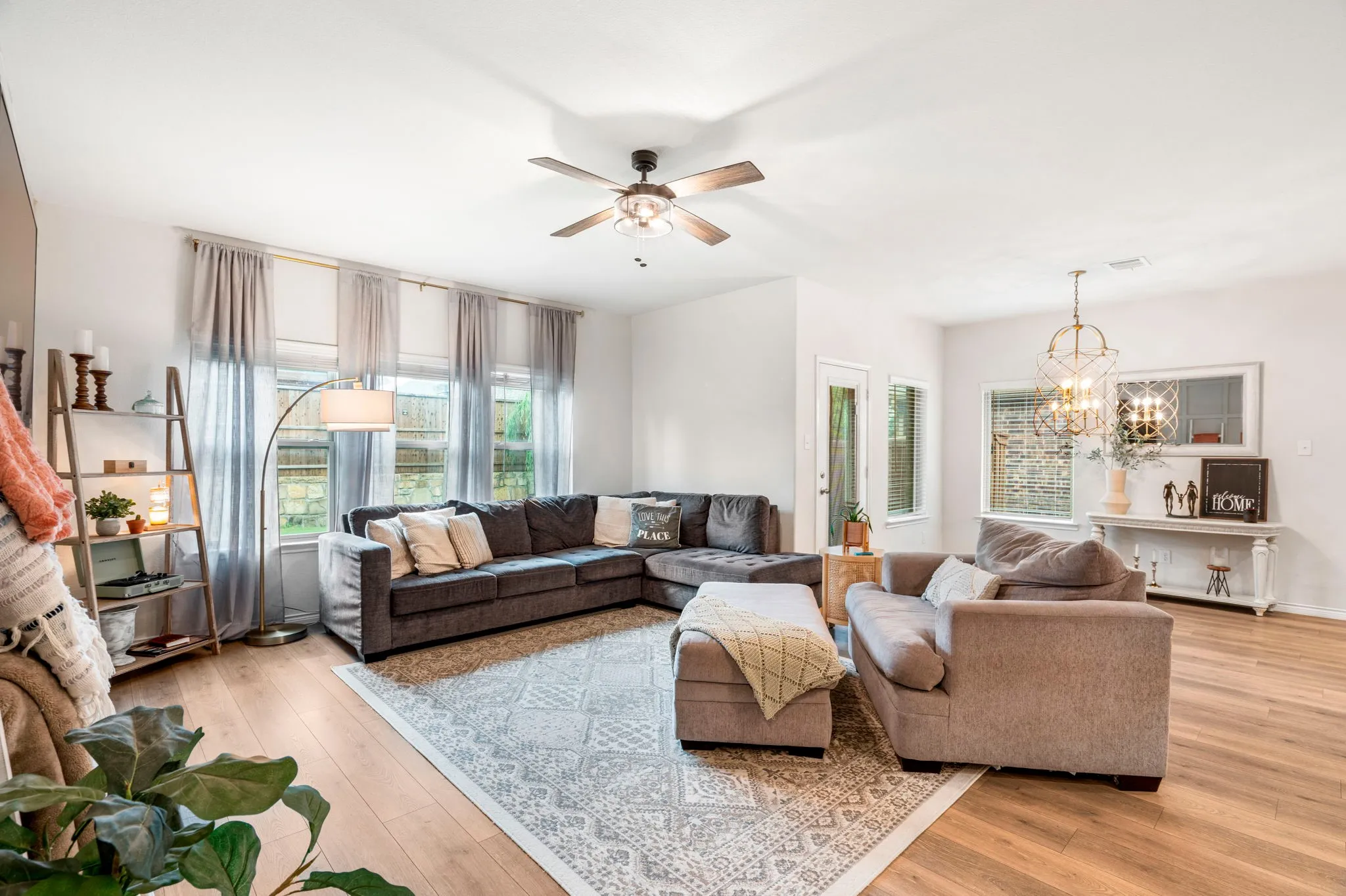 Spacious living area featuring light wood-finish flooring, a contemporary ceiling fan, and multiple windows providing natural illumination