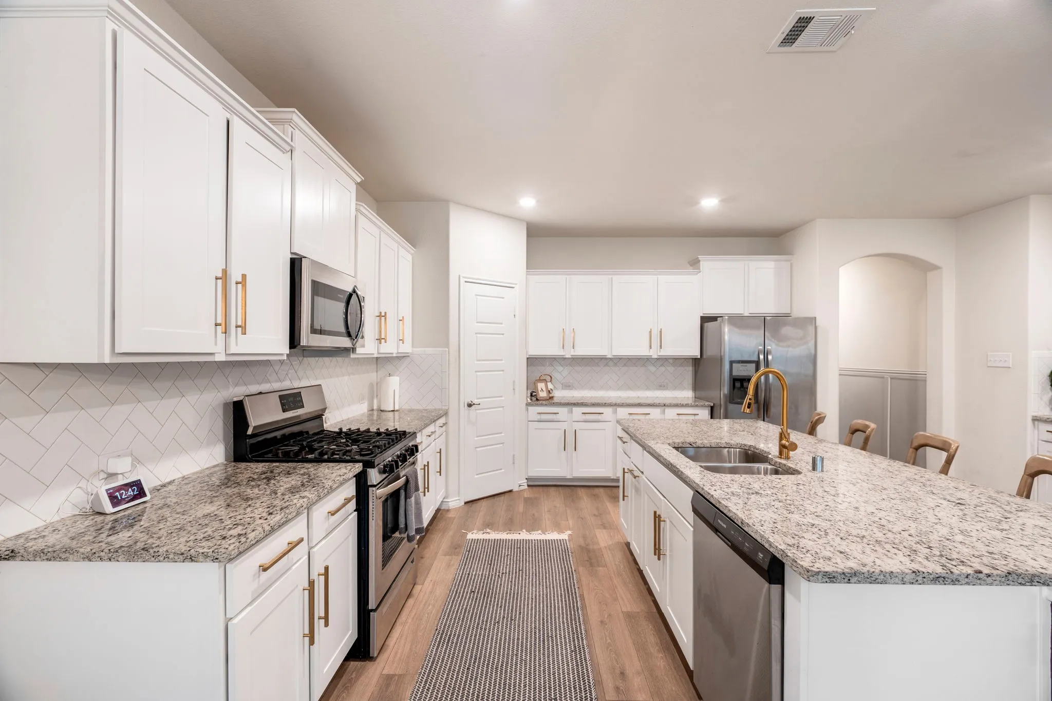 Kitchen featuring light-toned cabinetry with gold-toned hardware, stone countertops, stainless steel appliances, and a subway tile backsplash