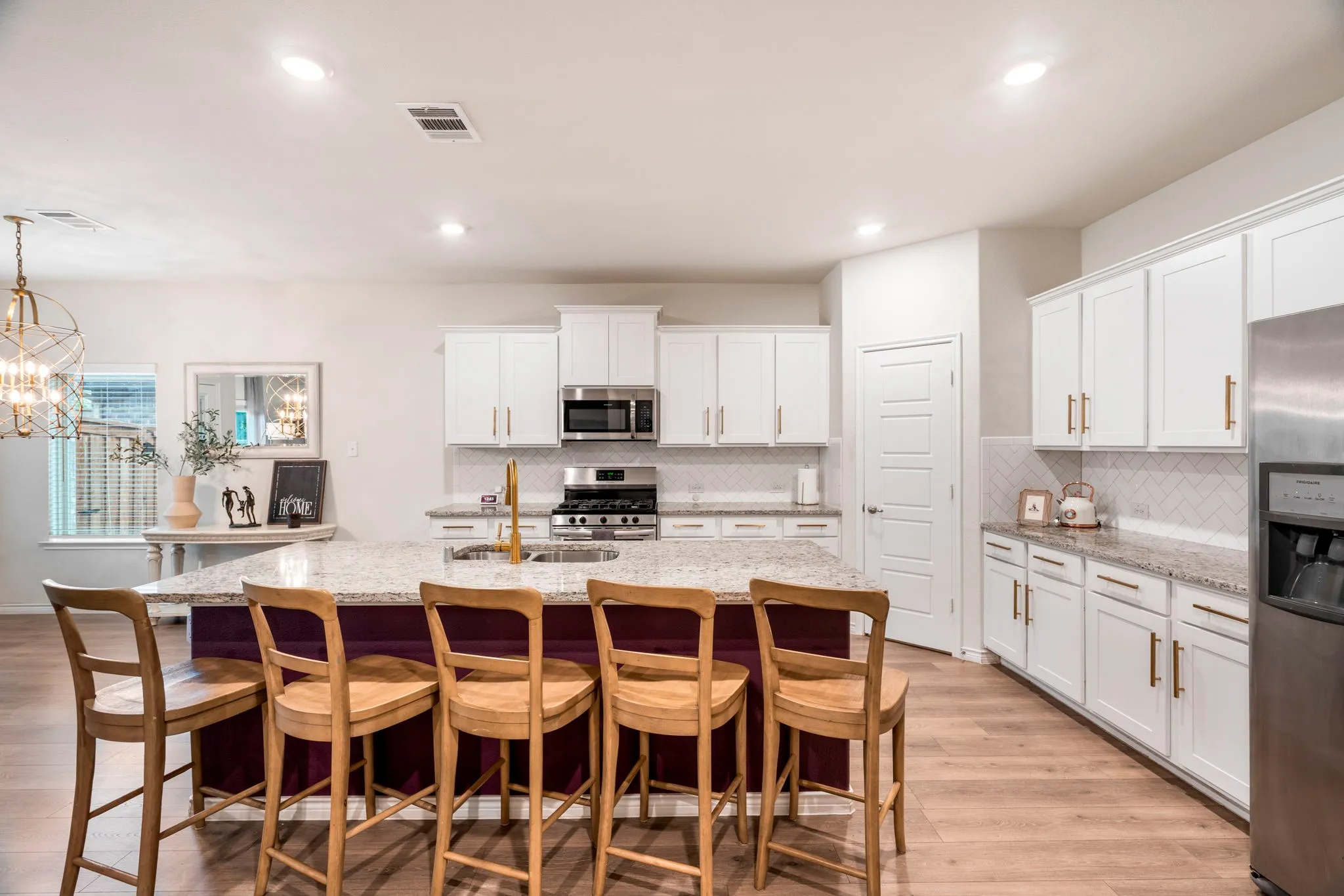 Kitchen featuring a spacious island with a granite countertop, white cabinetry with gold-toned hardware, stainless steel appliances, a tile backsplash, and wood-finish flooring