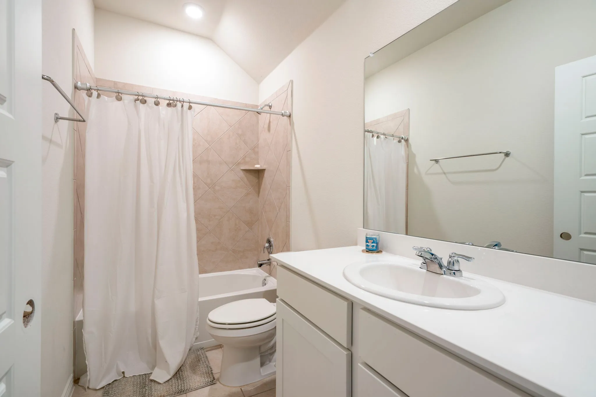 Bathroom featuring a white vanity with an integrated sink, a large wall-mounted mirror, and a tiled shower/tub combination with a built-in shelf