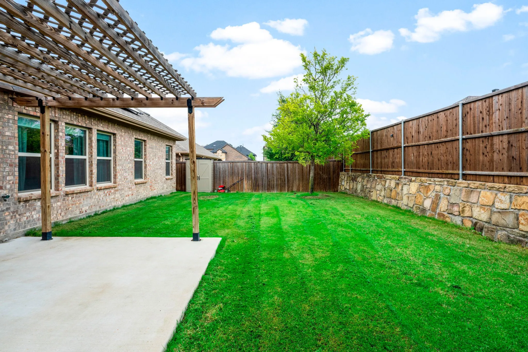 Spacious backyard featuring a pergola-covered patio, natural stone retaining wall, privacy fencing, and a mature tree