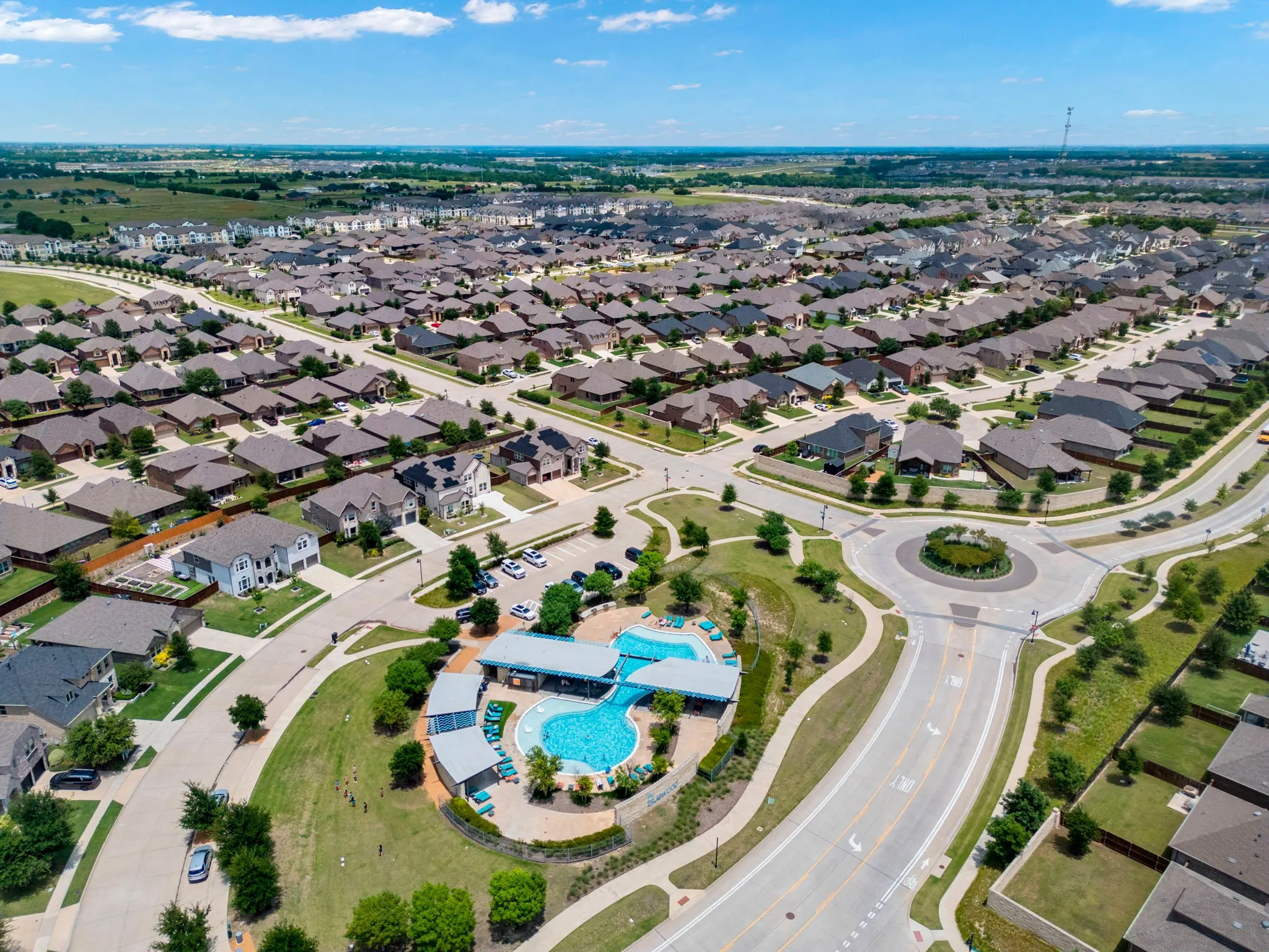 Expansive residential development featuring a large community pool, circular drive with landscaping, and numerous single-family homes