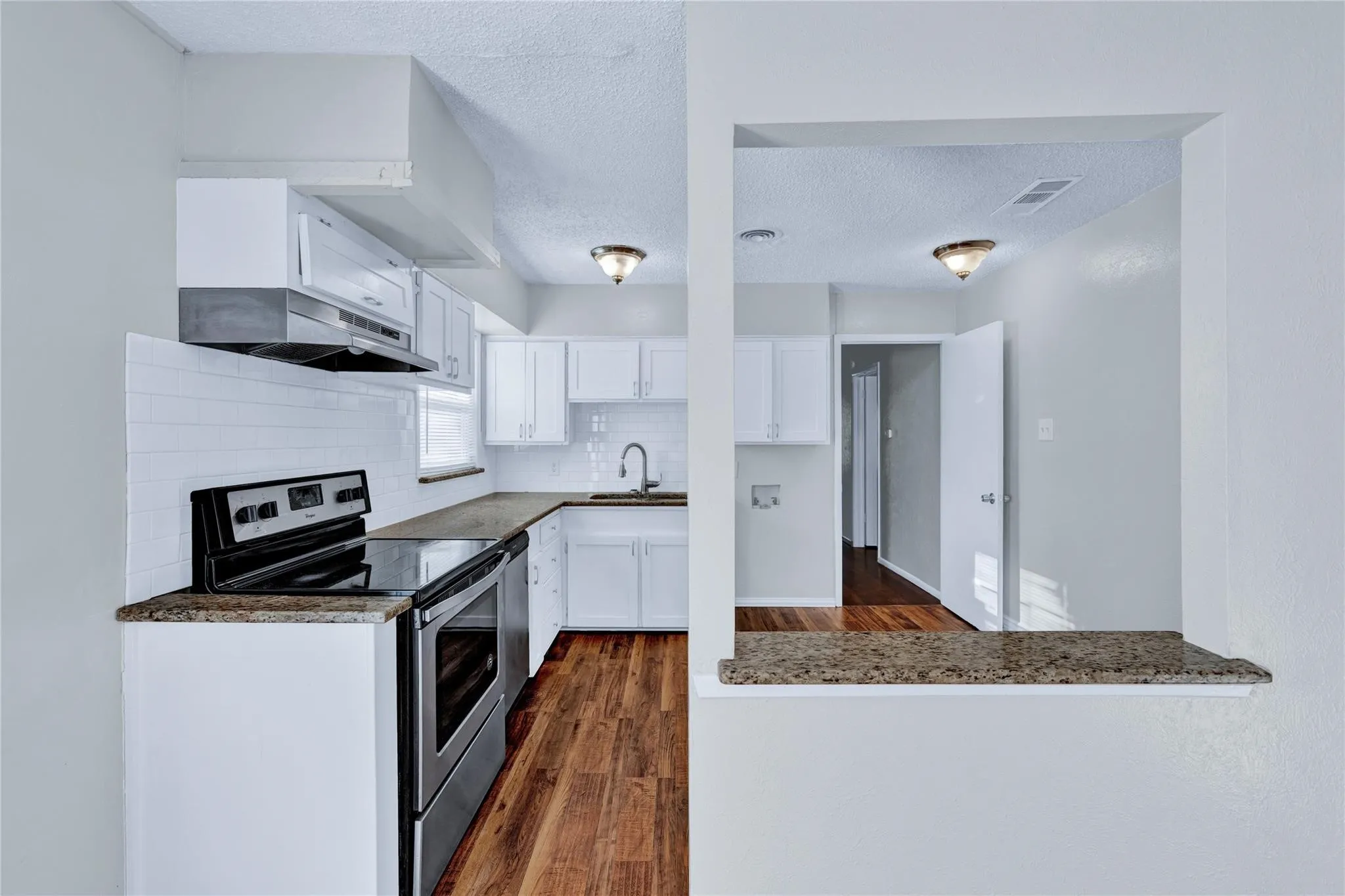 Kitchen featuring white cabinetry, subway tile backsplash, stainless steel appliances, wood-finish flooring, and a pass-through counter with a stone-finish surface