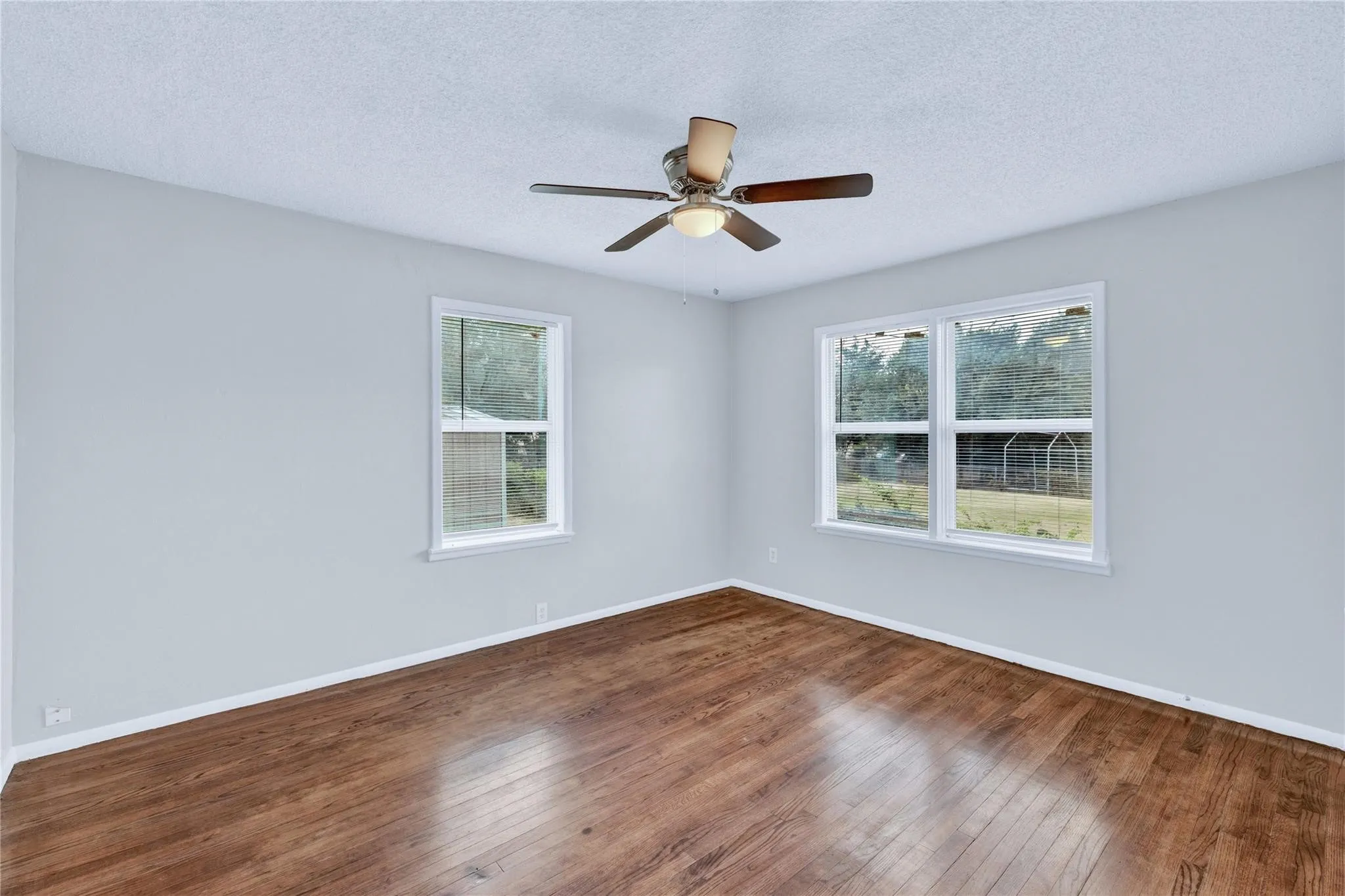 Spacious room featuring wood-finish flooring, light grey walls, and a ceiling fan with integrated lighting