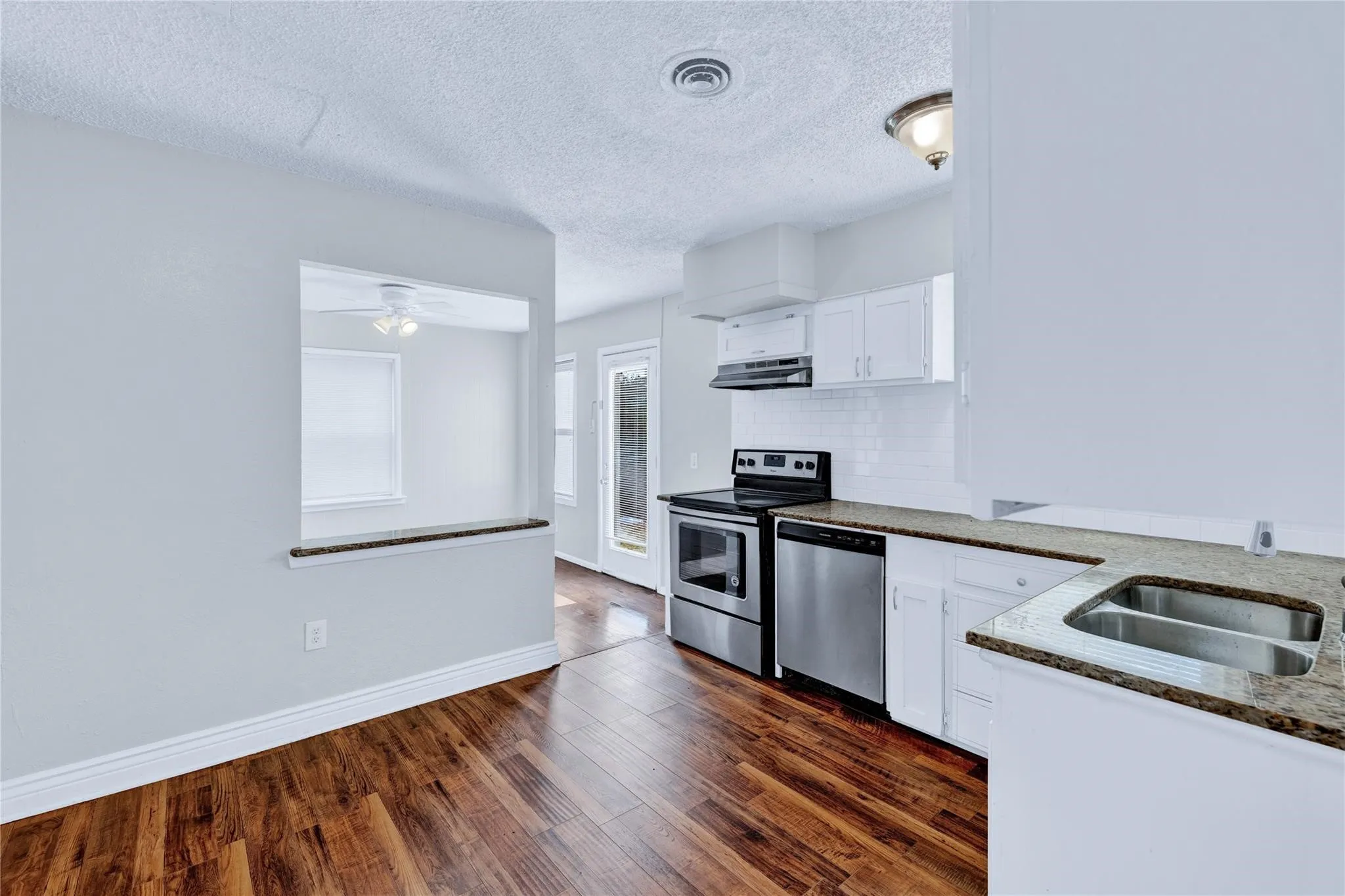 Kitchen featuring wood-finish flooring, white cabinetry, a double basin sink, and stainless steel appliances