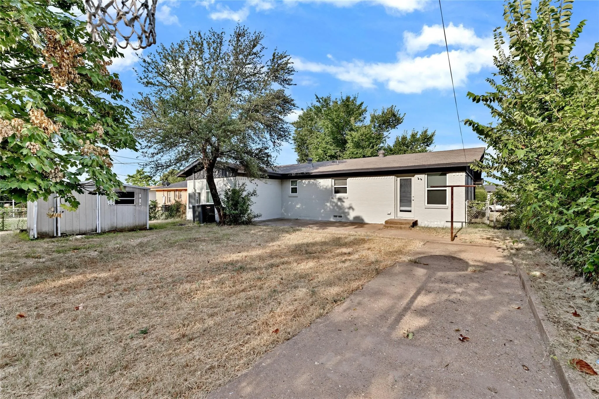 Rear exterior of a single-story residence featuring light-colored brick siding, a dark roofline, and a concrete patio