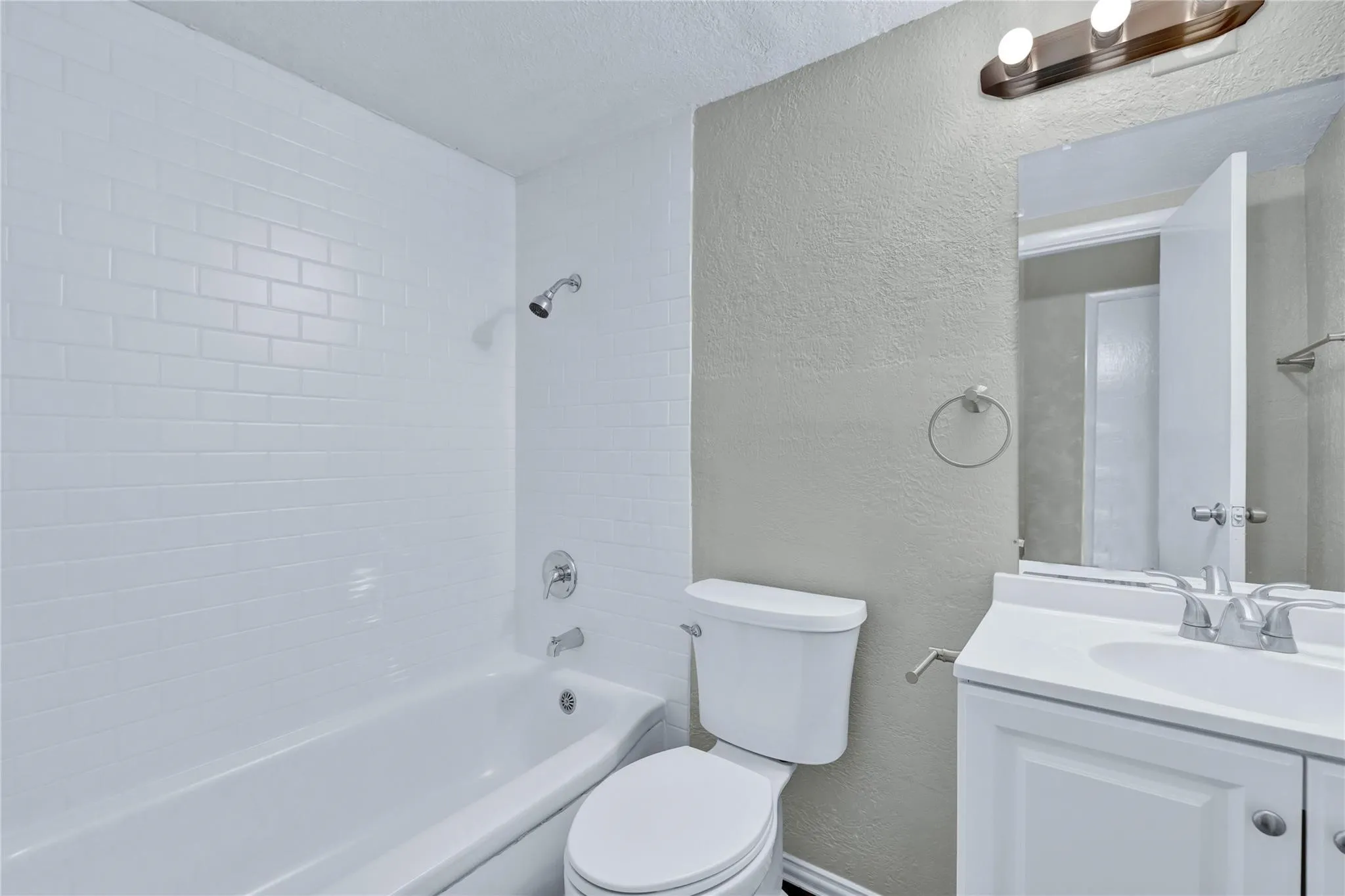 Bathroom featuring a white subway tile tub surround, chrome showerhead and fixtures, and a white toilet