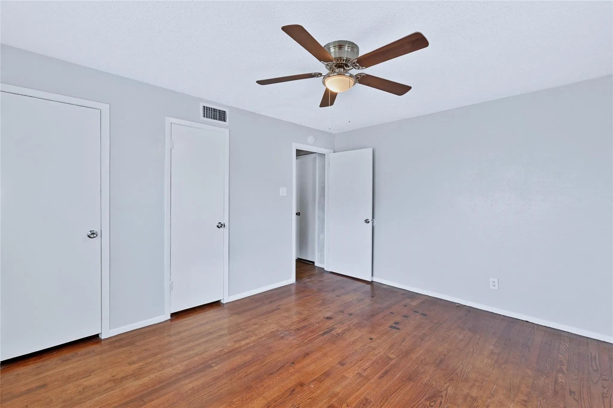 Room featuring wood-finish flooring, light grey walls, and a ceiling fan with integrated lighting