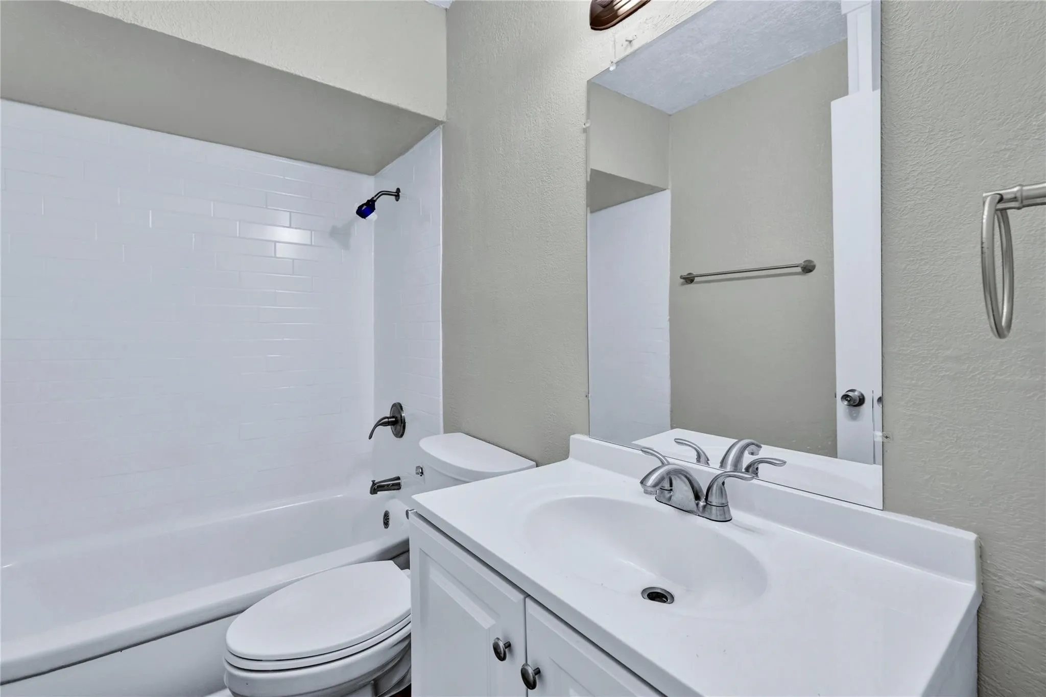 Bathroom featuring a white subway tile shower surround, a white vanity with an integrated sink, a chrome-finish faucet, a wall-mounted mirror, and a toilet