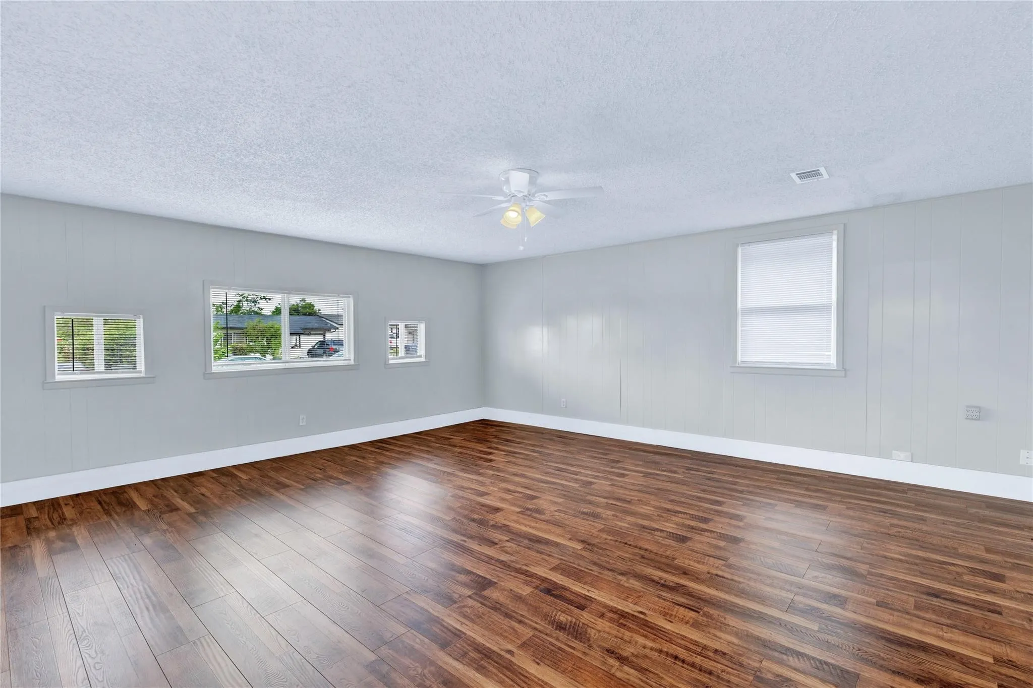 Spacious interior featuring wood-finish flooring, light gray walls, white trim, and multiple windows providing natural illumination