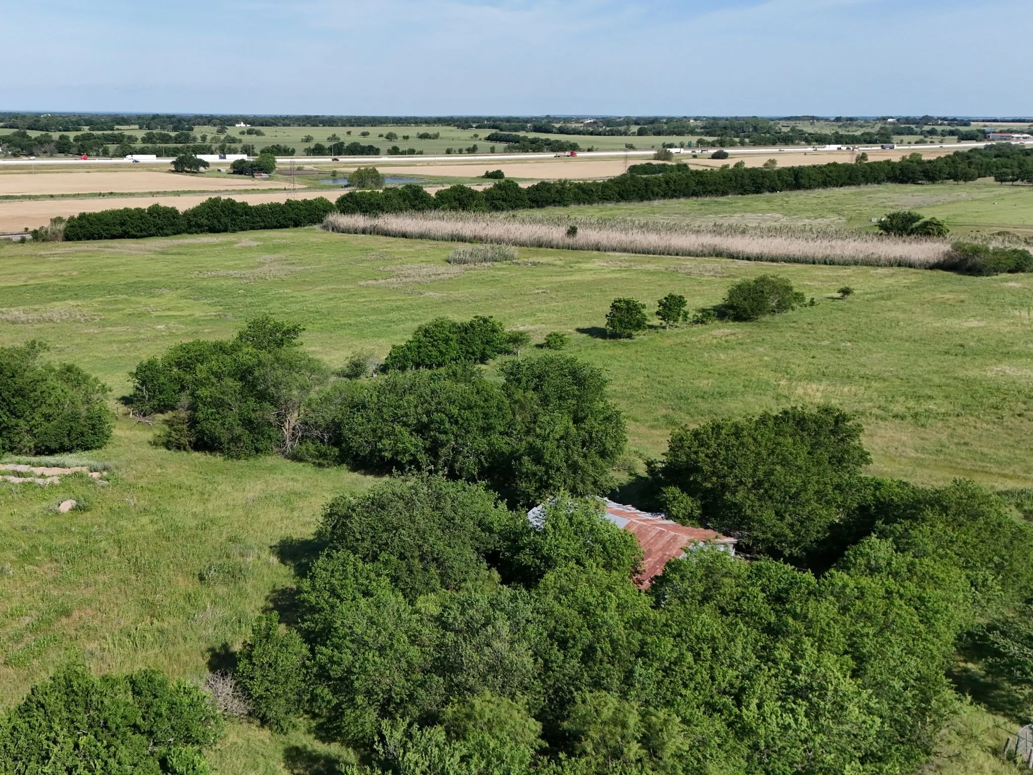 Expansive rural landscape featuring a single-story structure partially concealed by mature trees