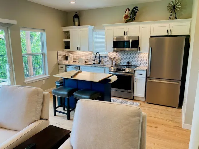Kitchen with stainless steel appliances, white cabinets, backsplash, light countertops, and a kitchen island