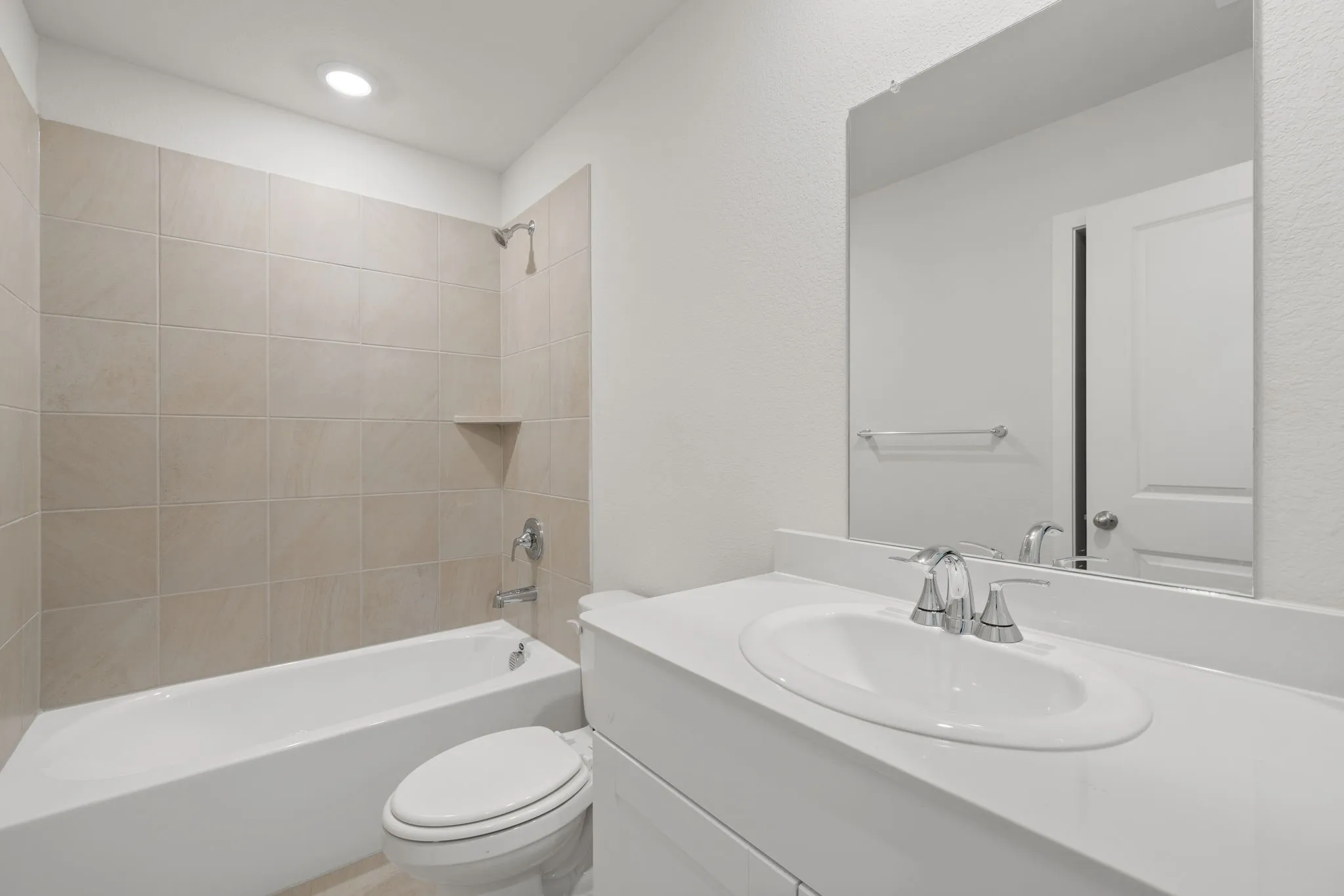 Bathroom featuring a tiled tub-shower combination with a built-in shelf, a white vanity with an integrated sink, polished chrome fixtures, and a frameless mirror