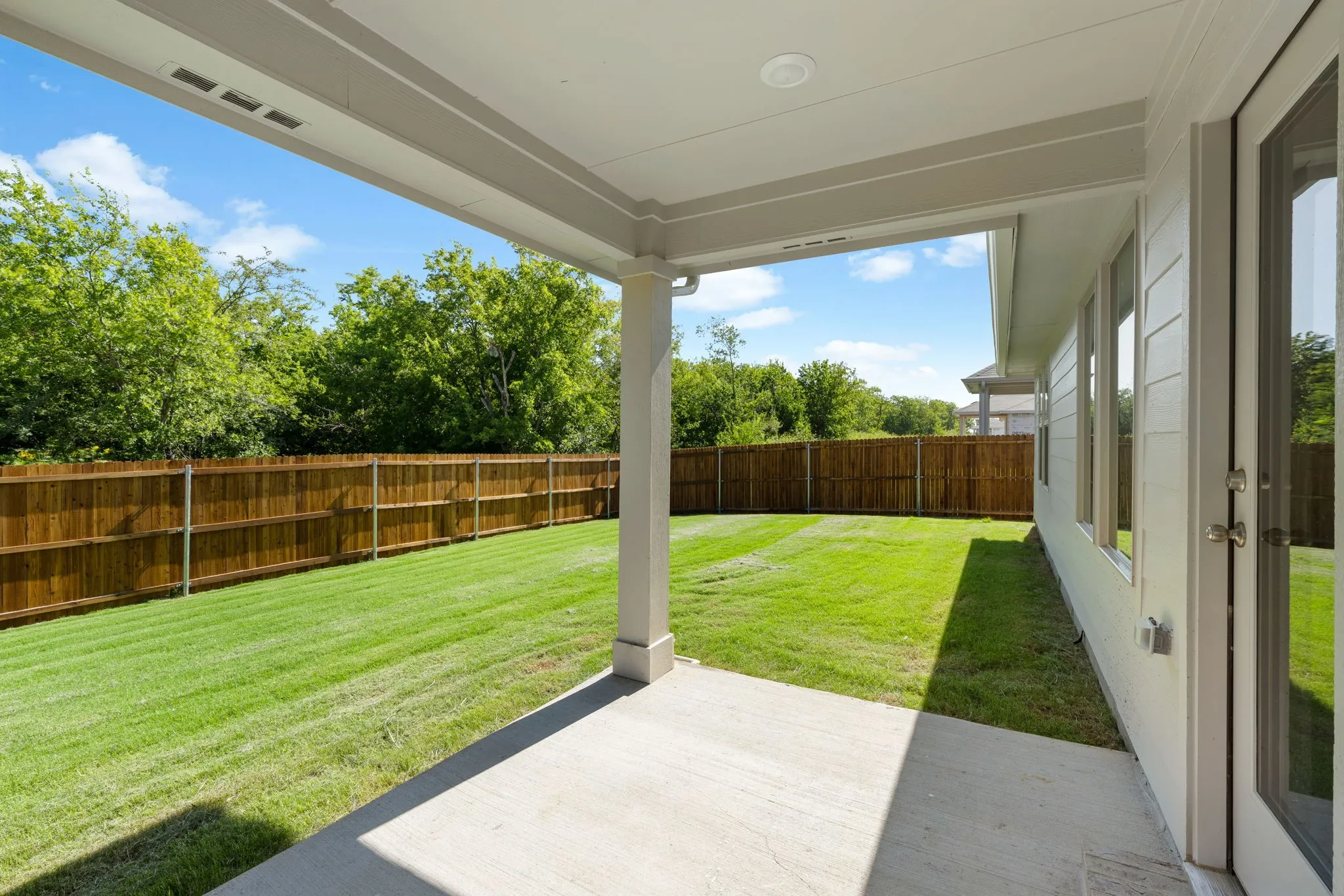 Expansive rear yard featuring a covered concrete patio, wood privacy fencing, and mature perimeter trees