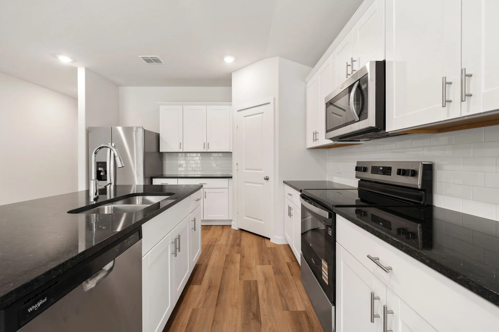 Contemporary kitchen featuring white cabinetry, dark countertops, wood-finish flooring, and stainless steel appliances including a refrigerator, range, microwave, and dishwasher