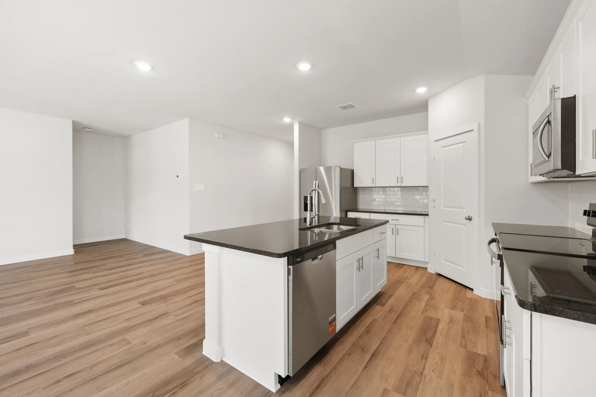 Open-concept kitchen featuring an island with a stainless steel sink and dishwasher, white cabinetry, dark countertops, and stainless steel appliances