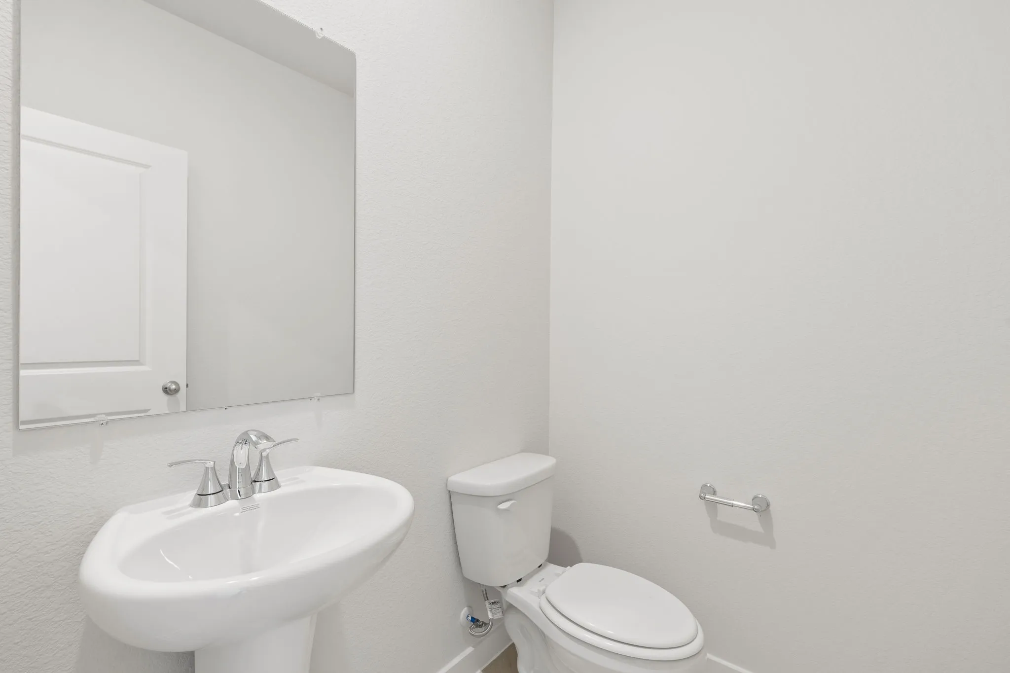 Pedestal sink with chrome faucet hardware, white toilet, and wall-mounted mirror