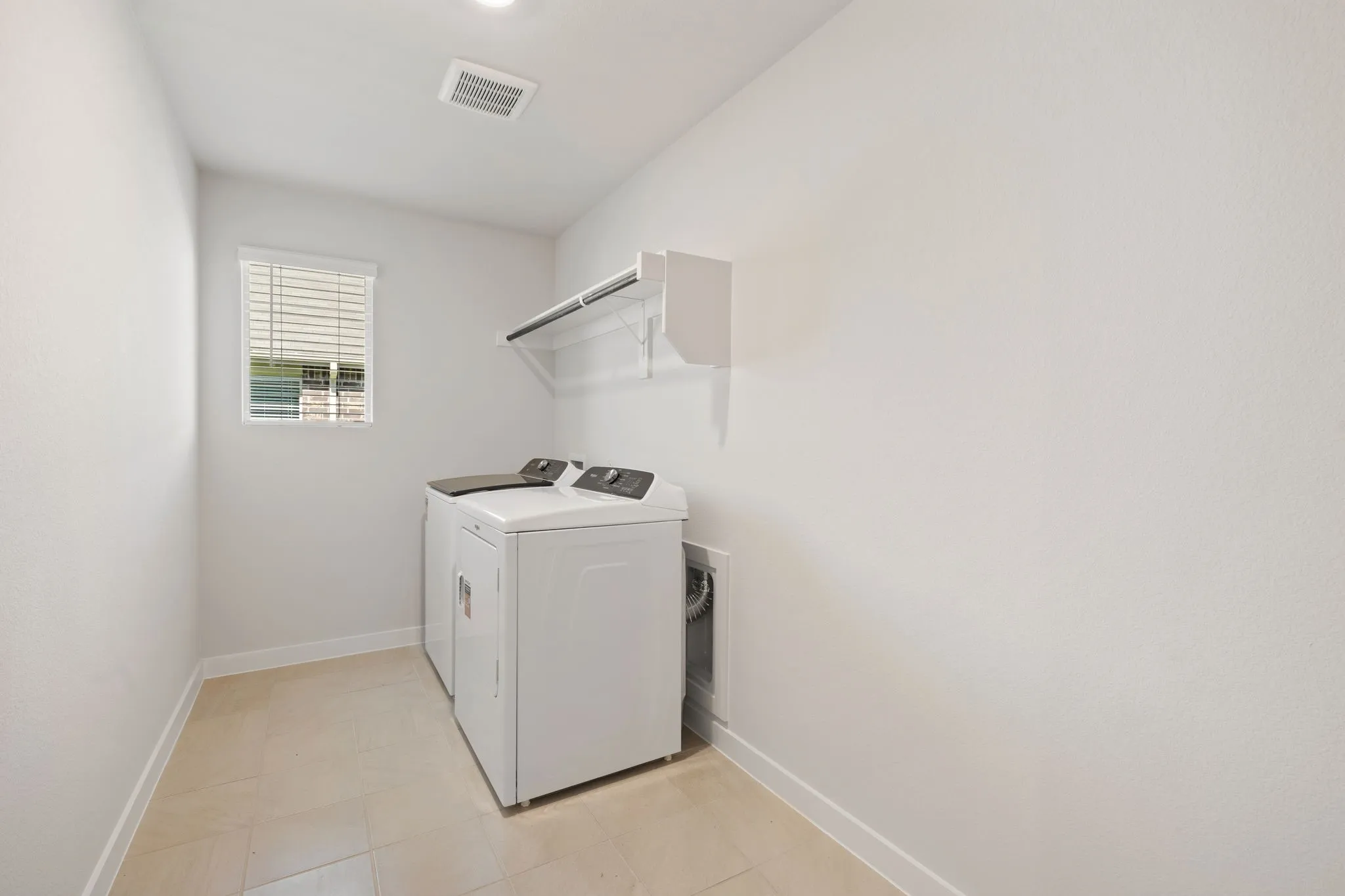 Dedicated utility space featuring tile flooring, a window with blinds, overhead shelving, and a built-in hanging rod