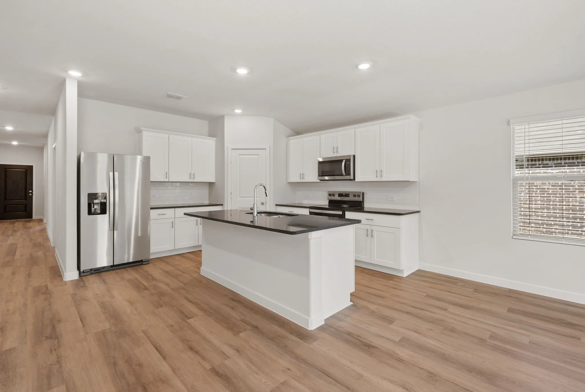 Open-concept kitchen featuring an island with a sink, white cabinetry, dark countertops, stainless steel appliances, and wood-finish flooring