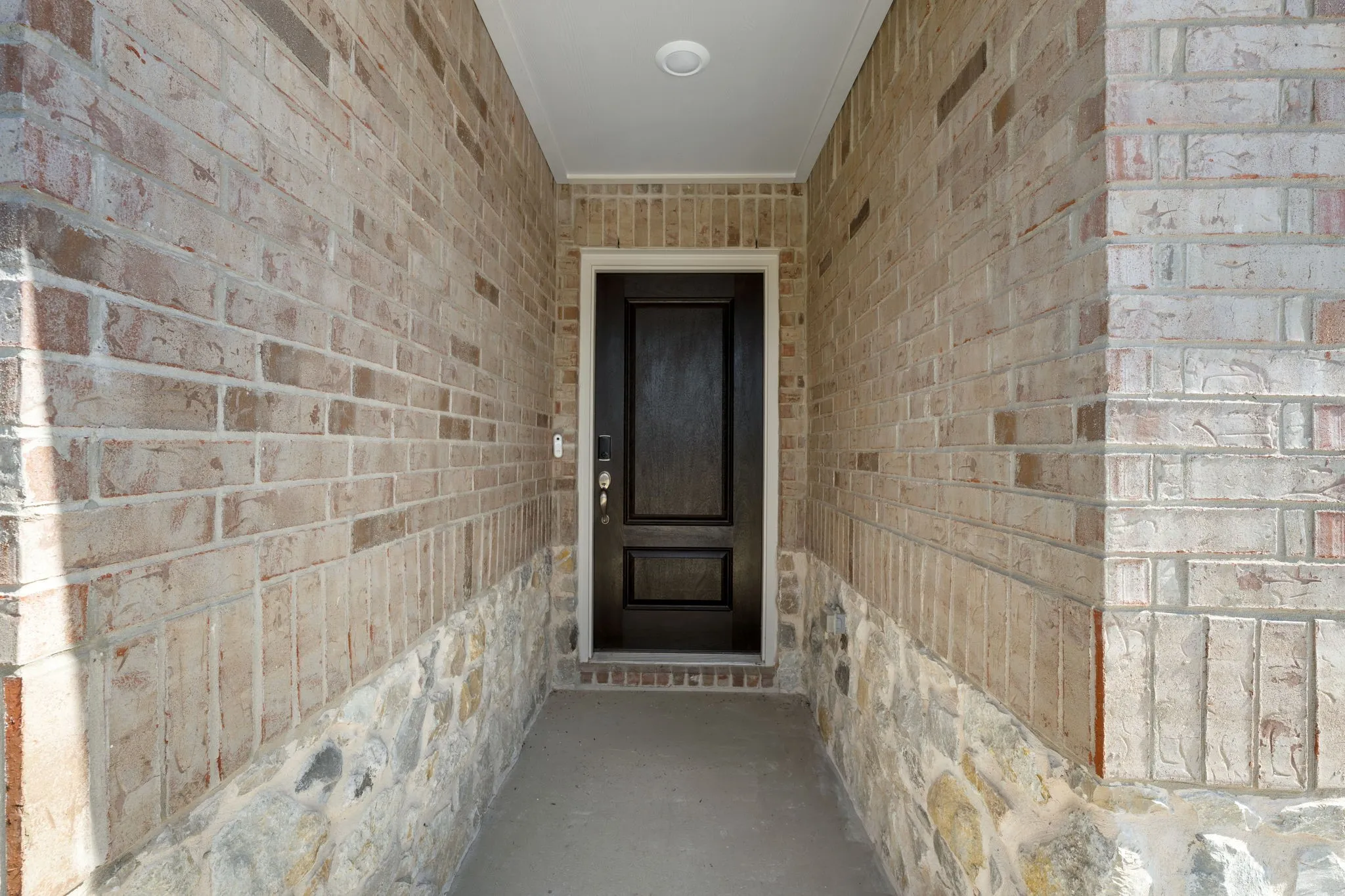 Covered entryway featuring a dark paneled door, brick facade, stone detailing, and recessed lighting
