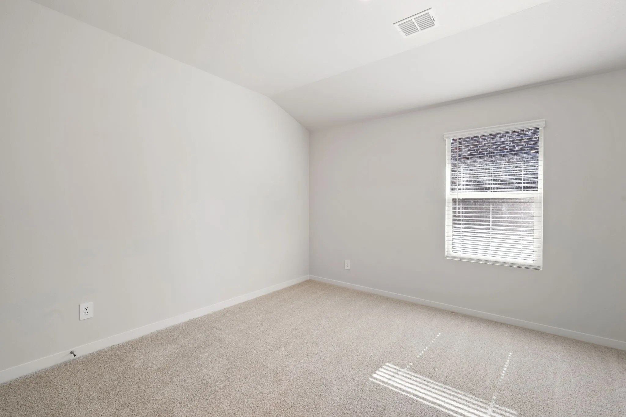 Neutral tone walls with white baseboards frame a window featuring white blinds